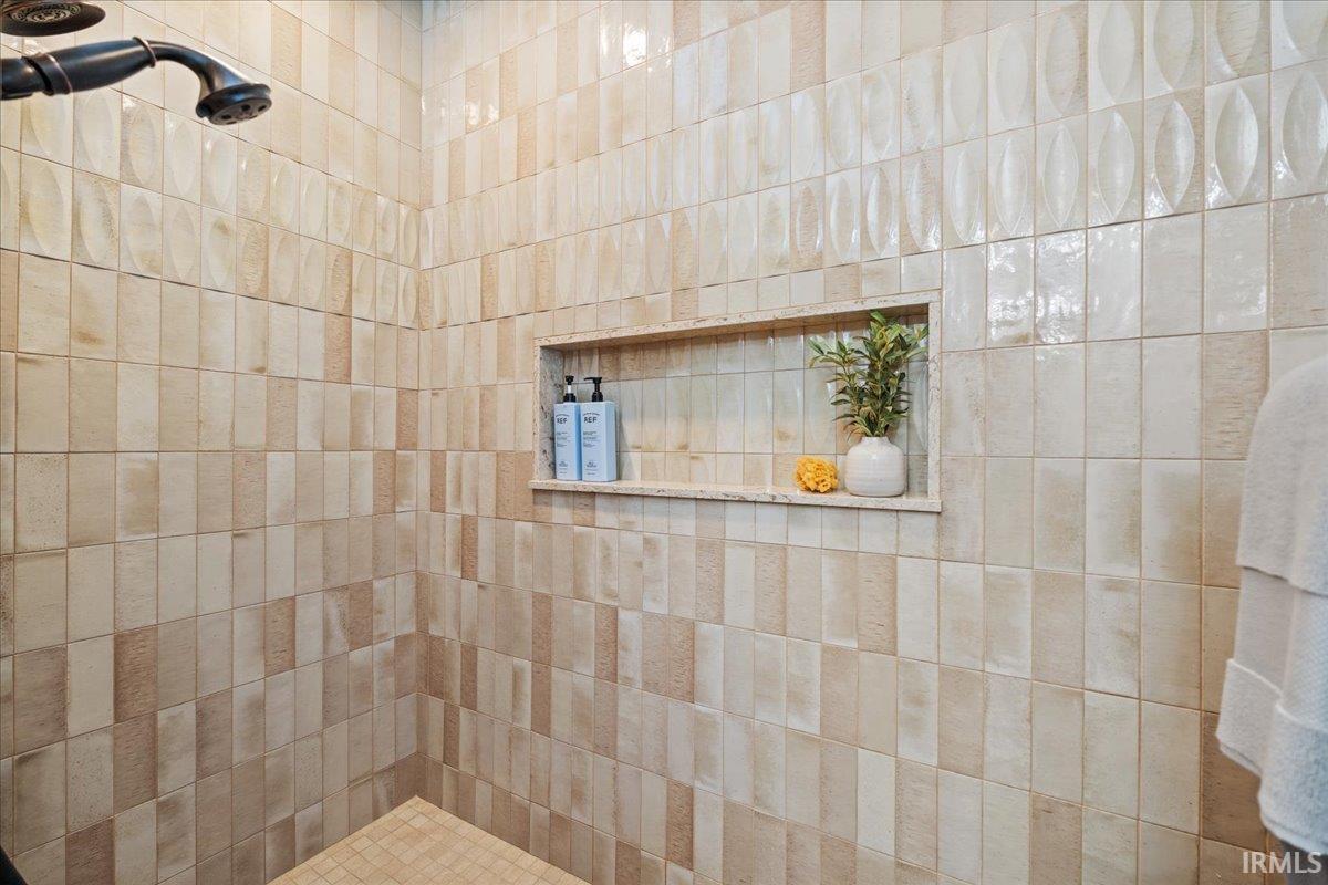 Expansive primary bedroom bath walk in tiled shower enclosure featuring a dark bronze shower head and a recessed niche