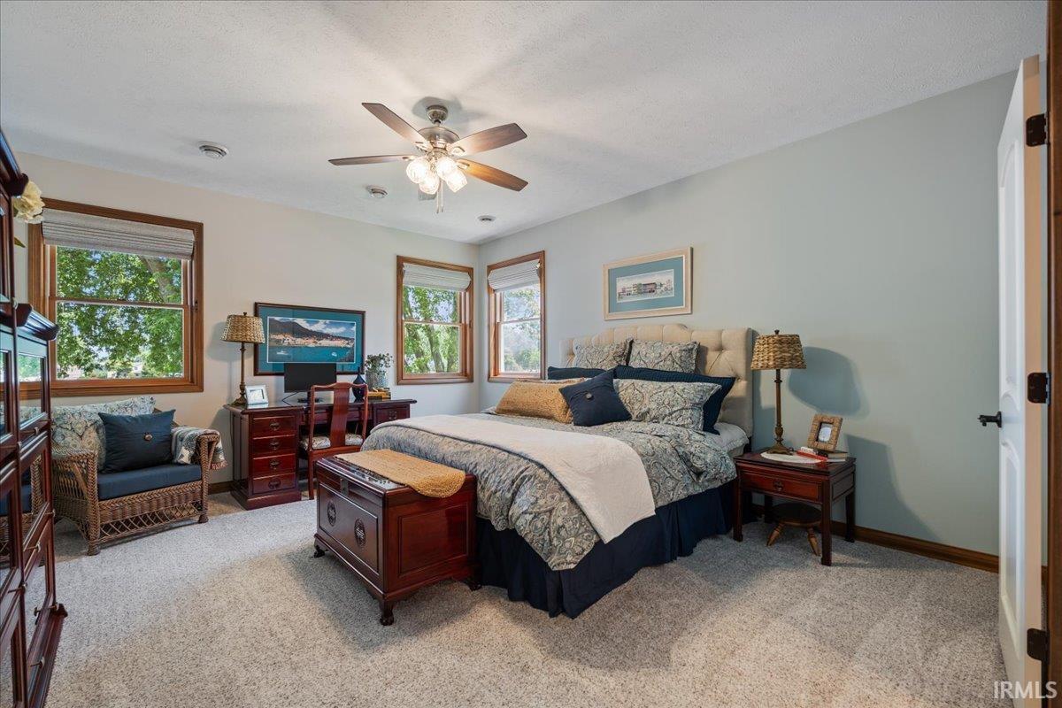 Spacious room featuring light-colored carpeting, multiple windows with wood trim, a ceiling fan with integrated lighting, and recessed ceiling lights