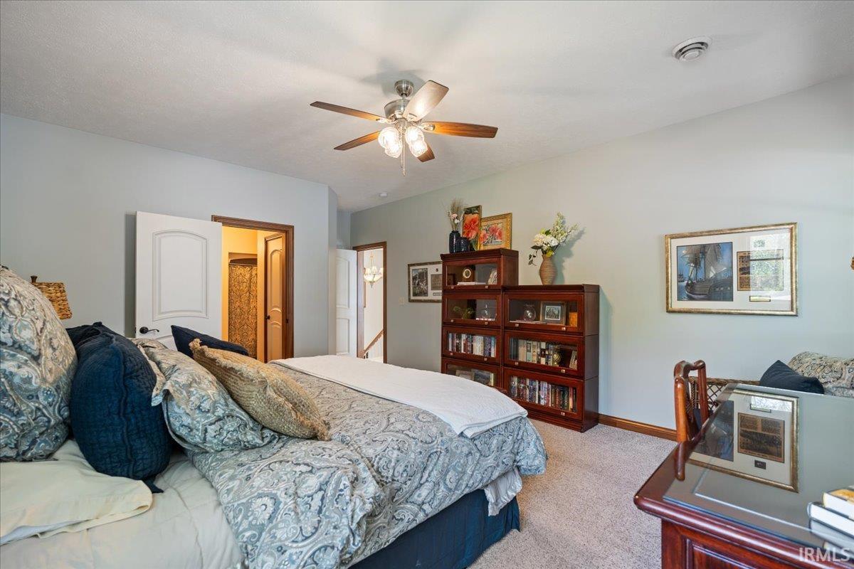 Carpeted room featuring a ceiling fan with light fixture, light gray wall paint, and a built-in wooden bookcase