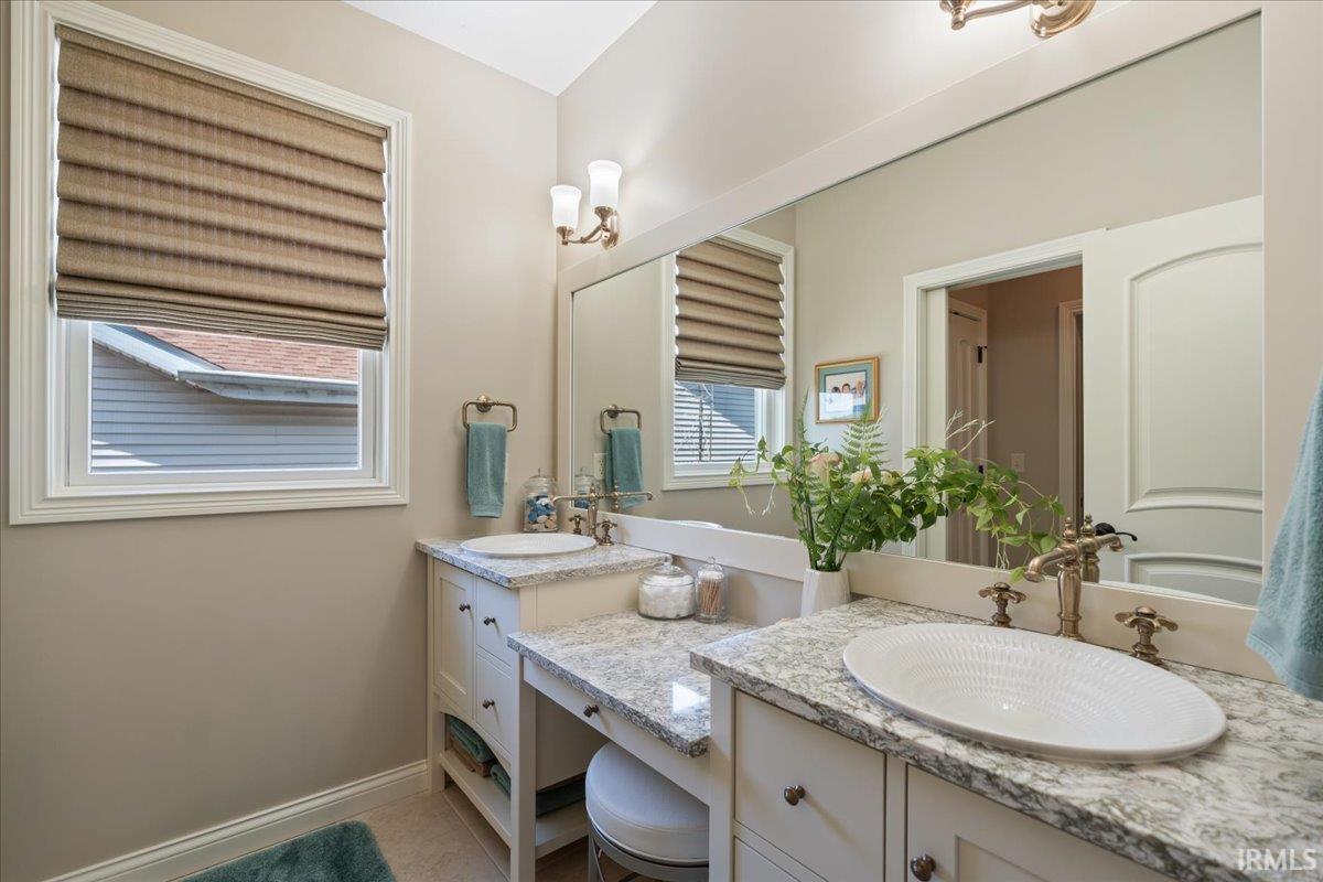 Dual vanity featuring light-toned cabinetry, granite countertops, and two vessel sinks with bronze-finish fixtures