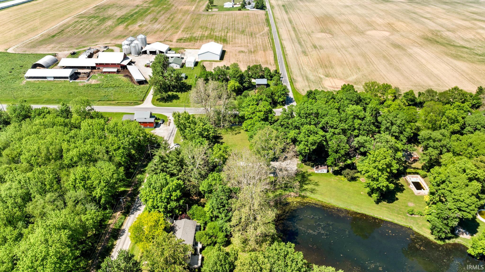 Aerial property overview featuring a private pond, expansive wooded areas, and agricultural land