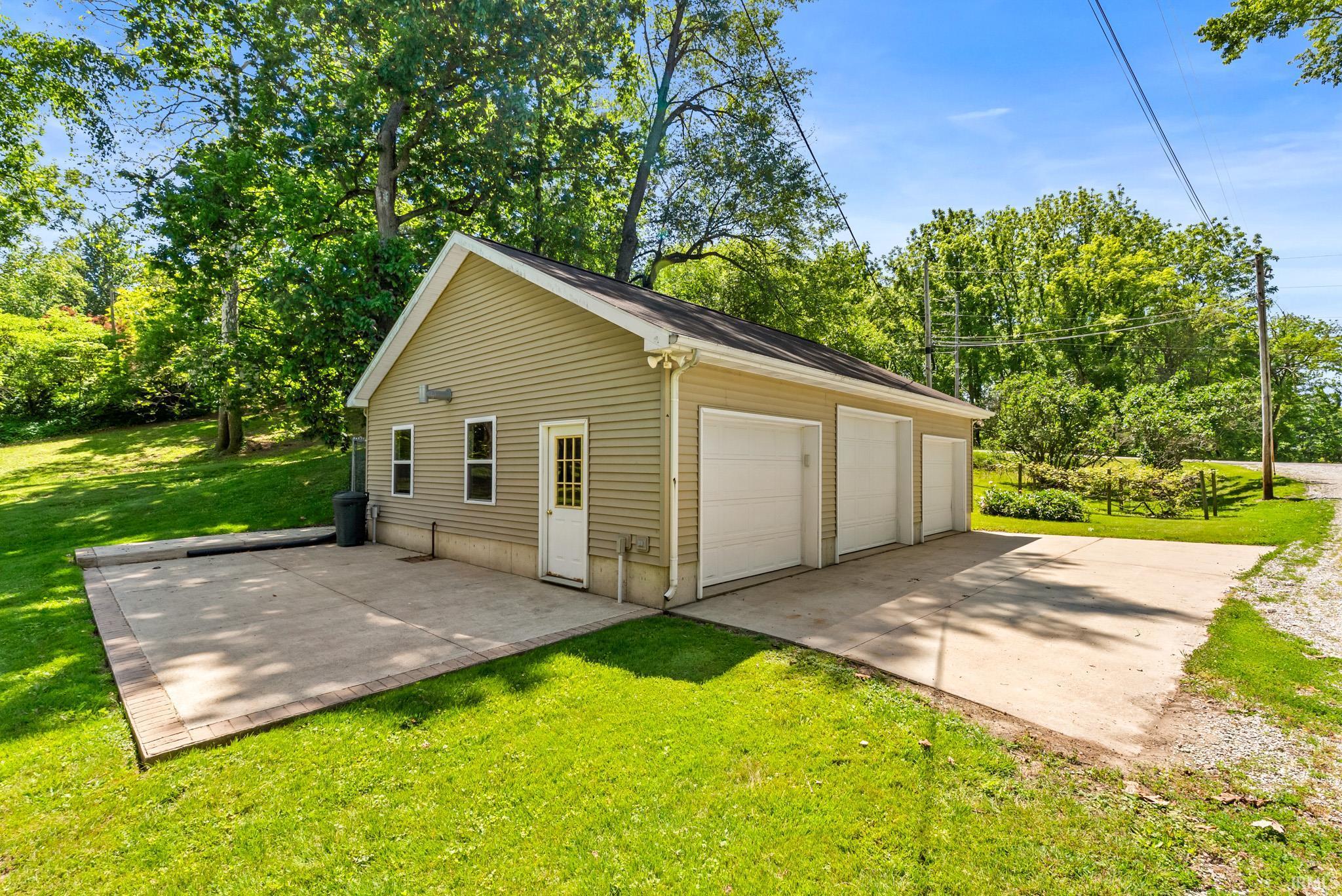 Detached three-car garage with light-colored siding, a gabled roof, and a side entry door