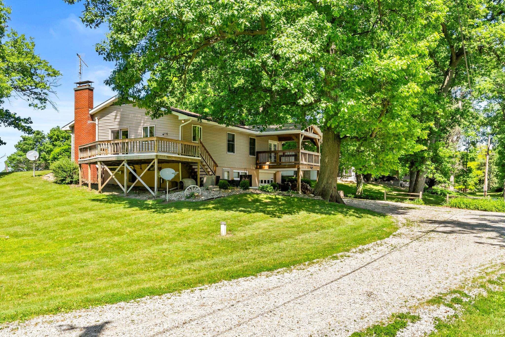 Expansive gravel driveway leading to a multi-level residence featuring light-colored siding