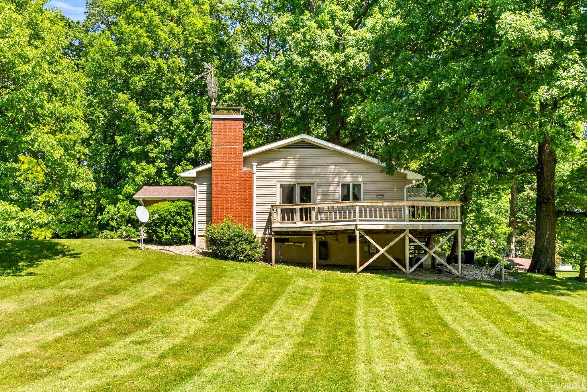 Spacious rear yard with striped lawn, mature trees, and a raised wooden deck