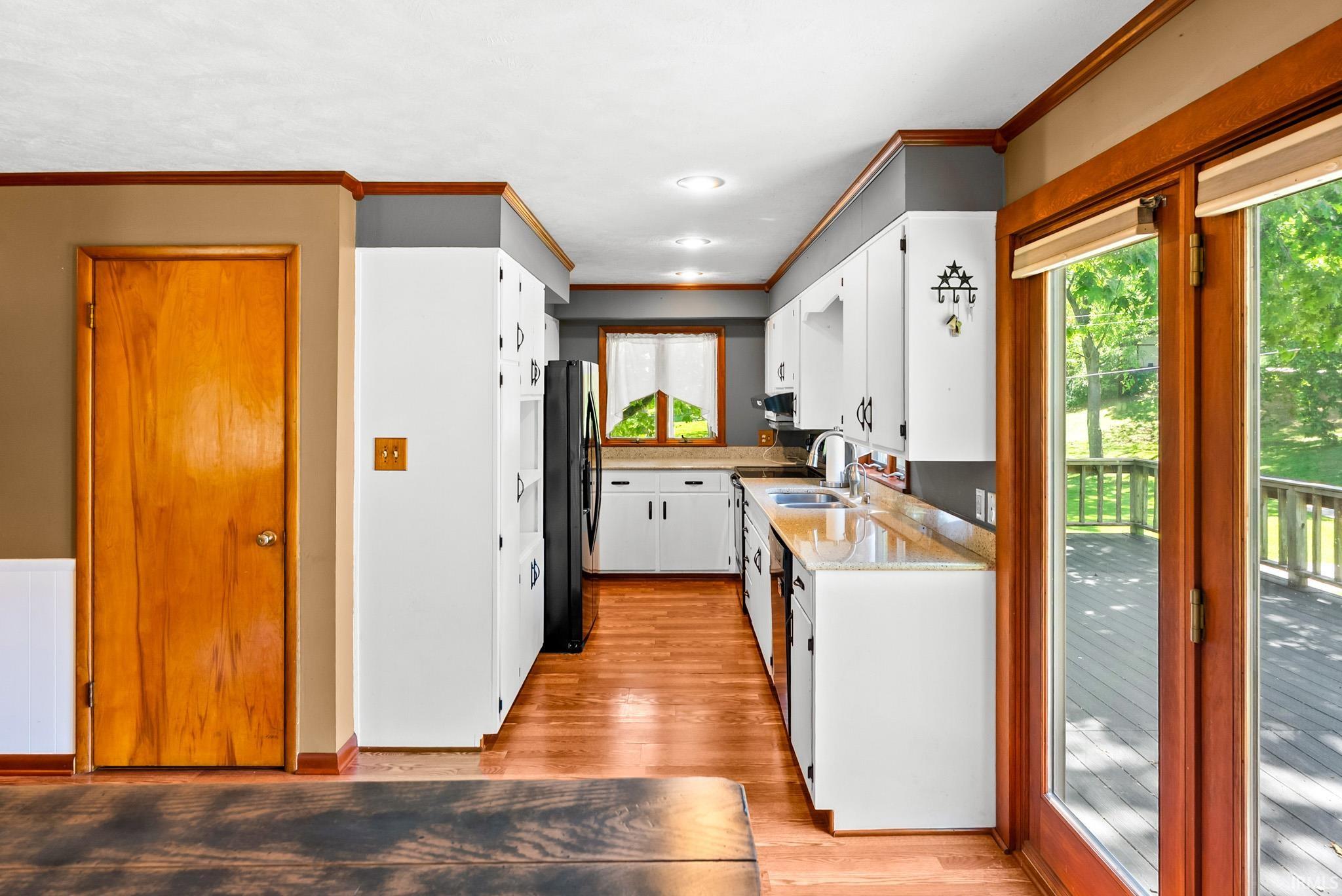 Galley kitchen featuring white cabinetry, light countertops, wood-finish flooring, recessed lighting, and a window overlooking exterior greenery
