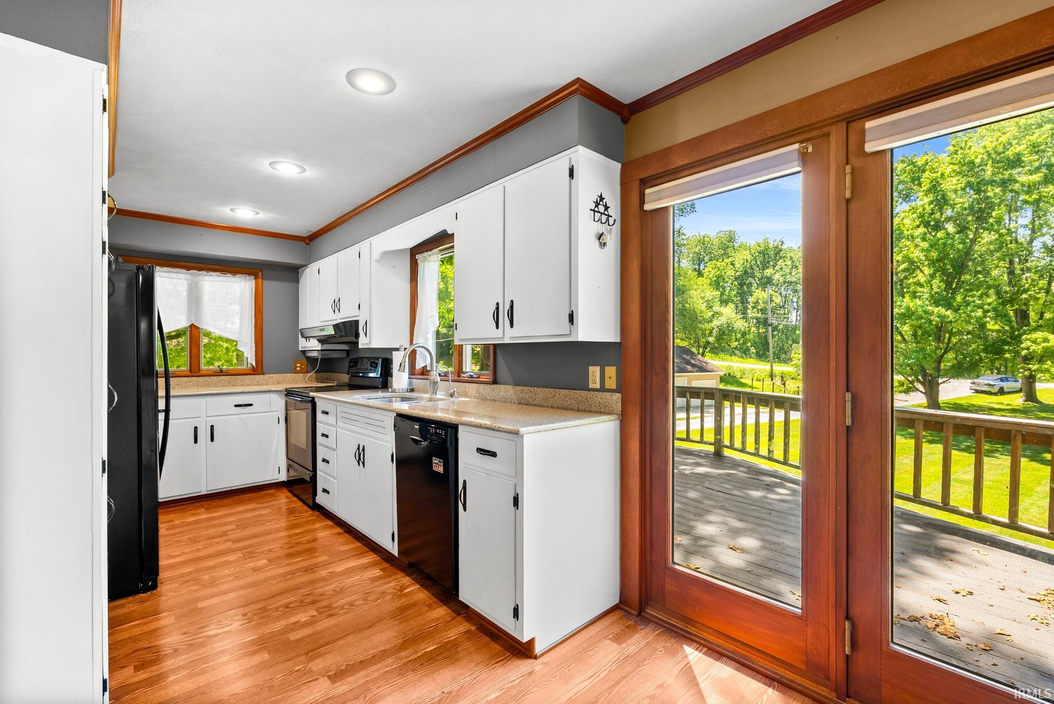 Kitchen featuring white cabinetry, light countertops, black appliances, and wood-finish flooring
