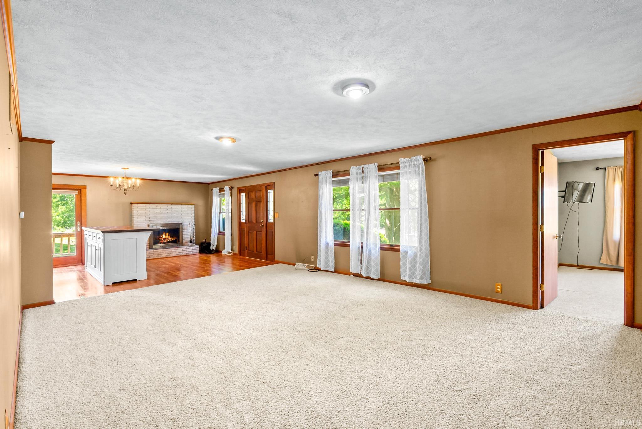 Spacious room featuring light-colored carpeting, multiple windows with white curtains, and a prominent brick fireplace