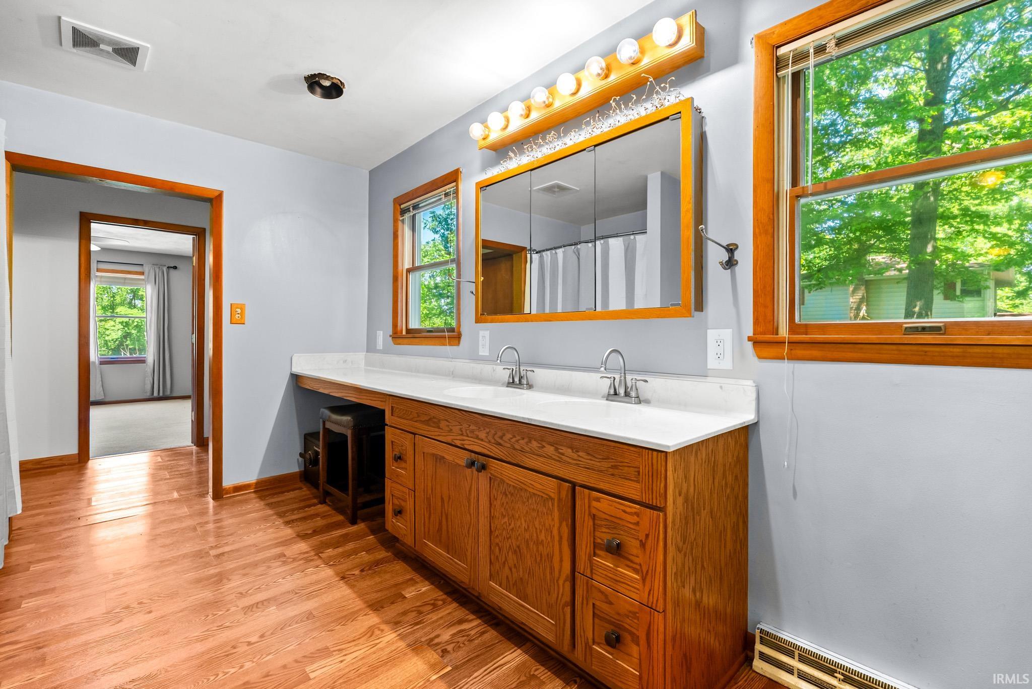Bathroom vanity featuring a light wood-finish double cabinet, white countertop with dual sinks, and a recessed medicine cabinet with overhead lighting