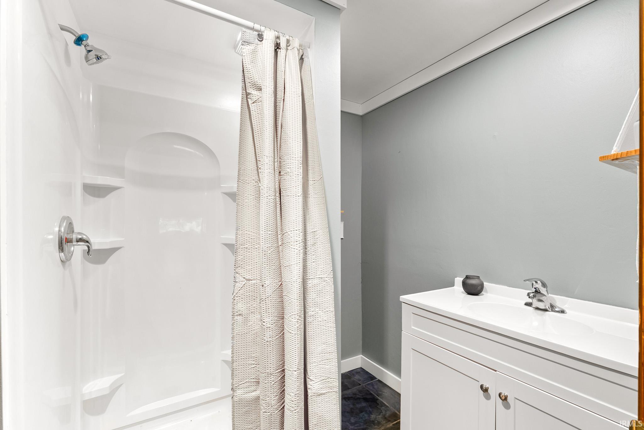 White shower surround with integrated shelving and chrome fixtures, accompanied by a white vanity with an integrated sink and chrome faucet