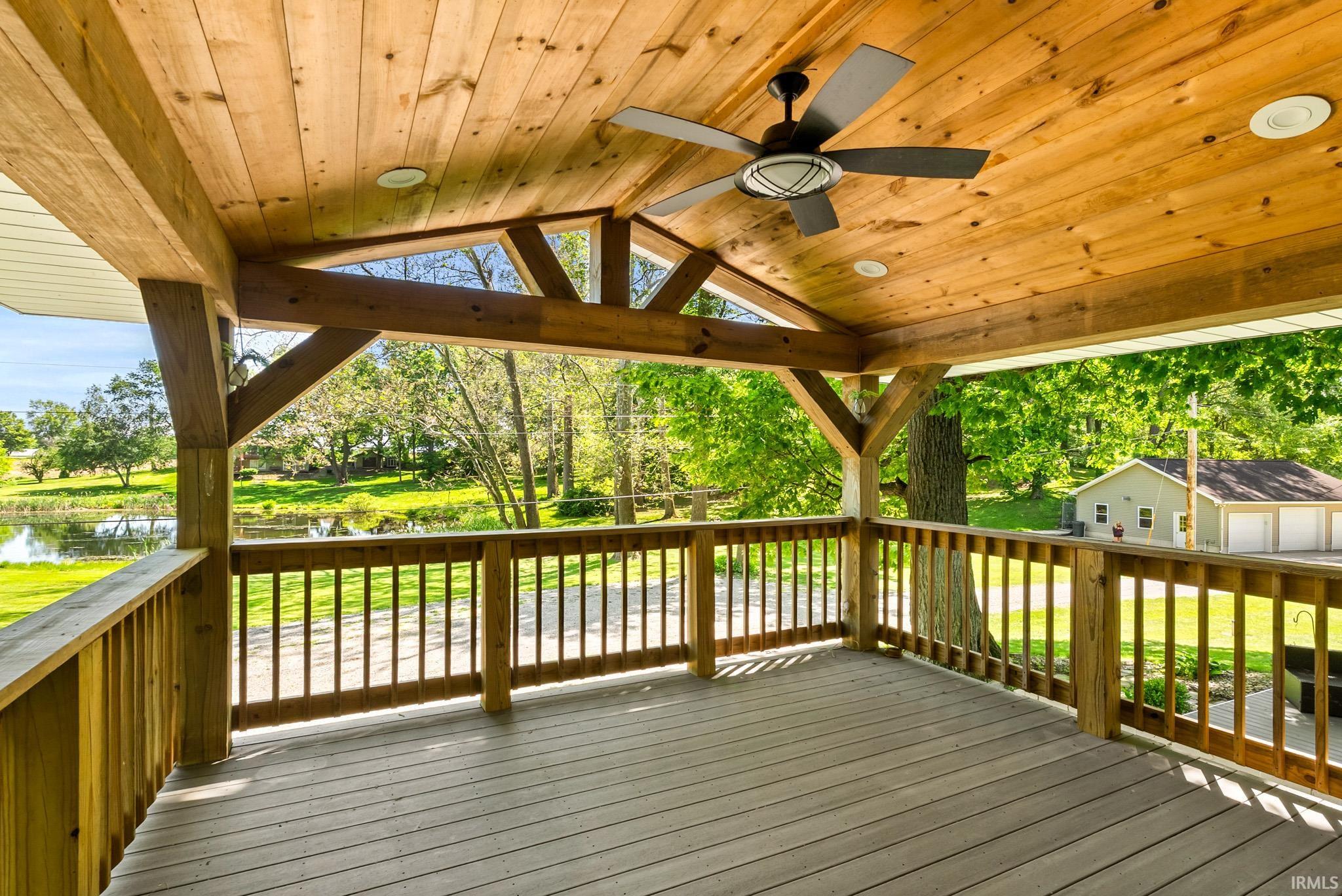Spacious covered deck featuring a natural wood ceiling, exposed wood beams, and a modern ceiling fan