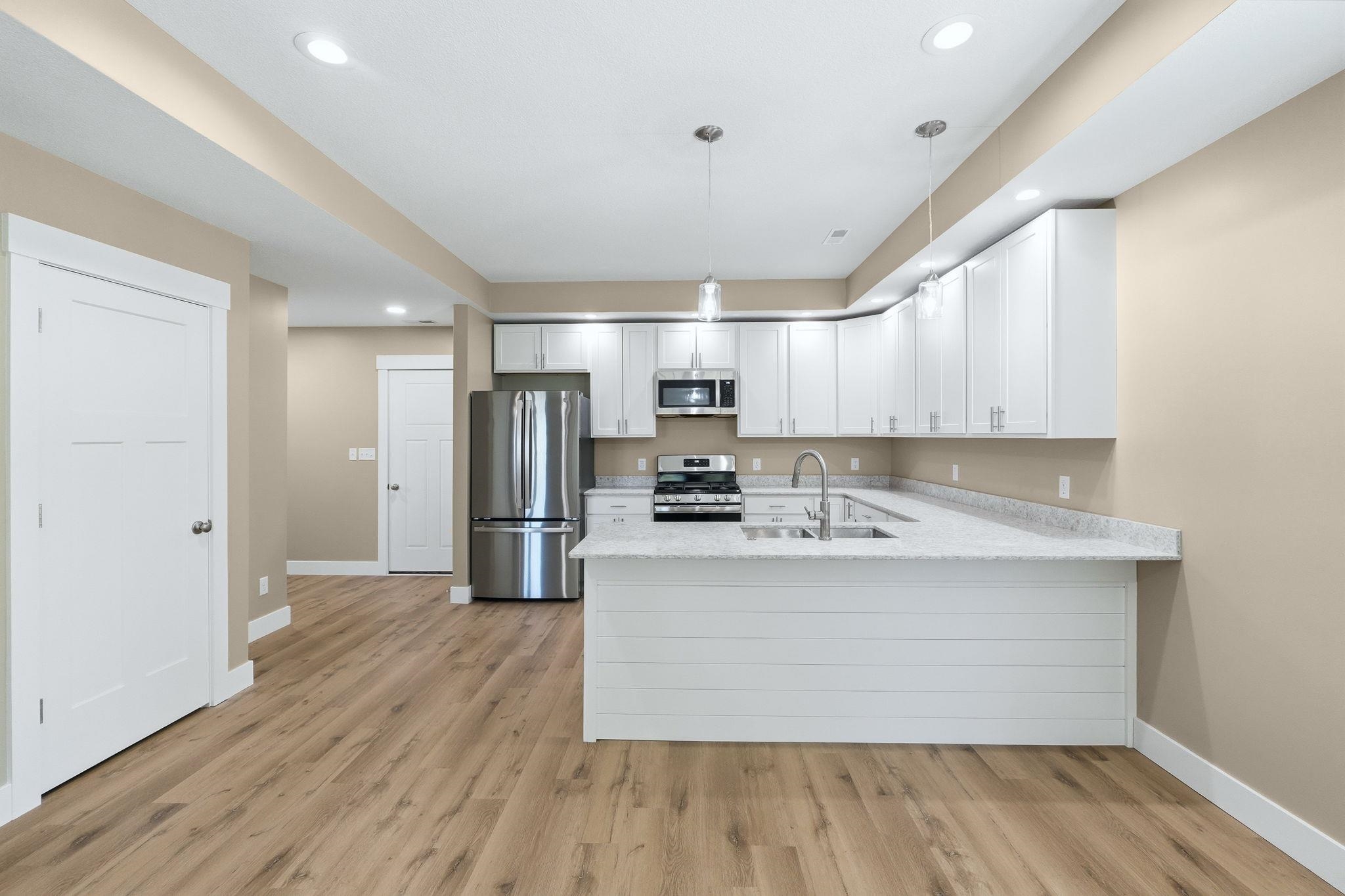 Modern kitchen featuring white cabinetry, stainless steel appliances, light-toned countertops, and wood-finish flooring