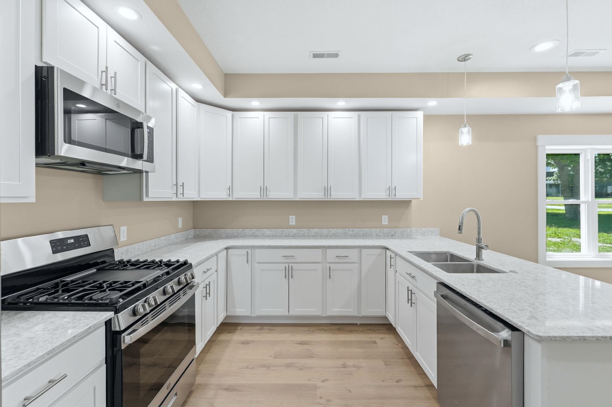 Modern kitchen featuring white cabinetry, light-toned countertops, stainless steel appliances, and wood-finish flooring