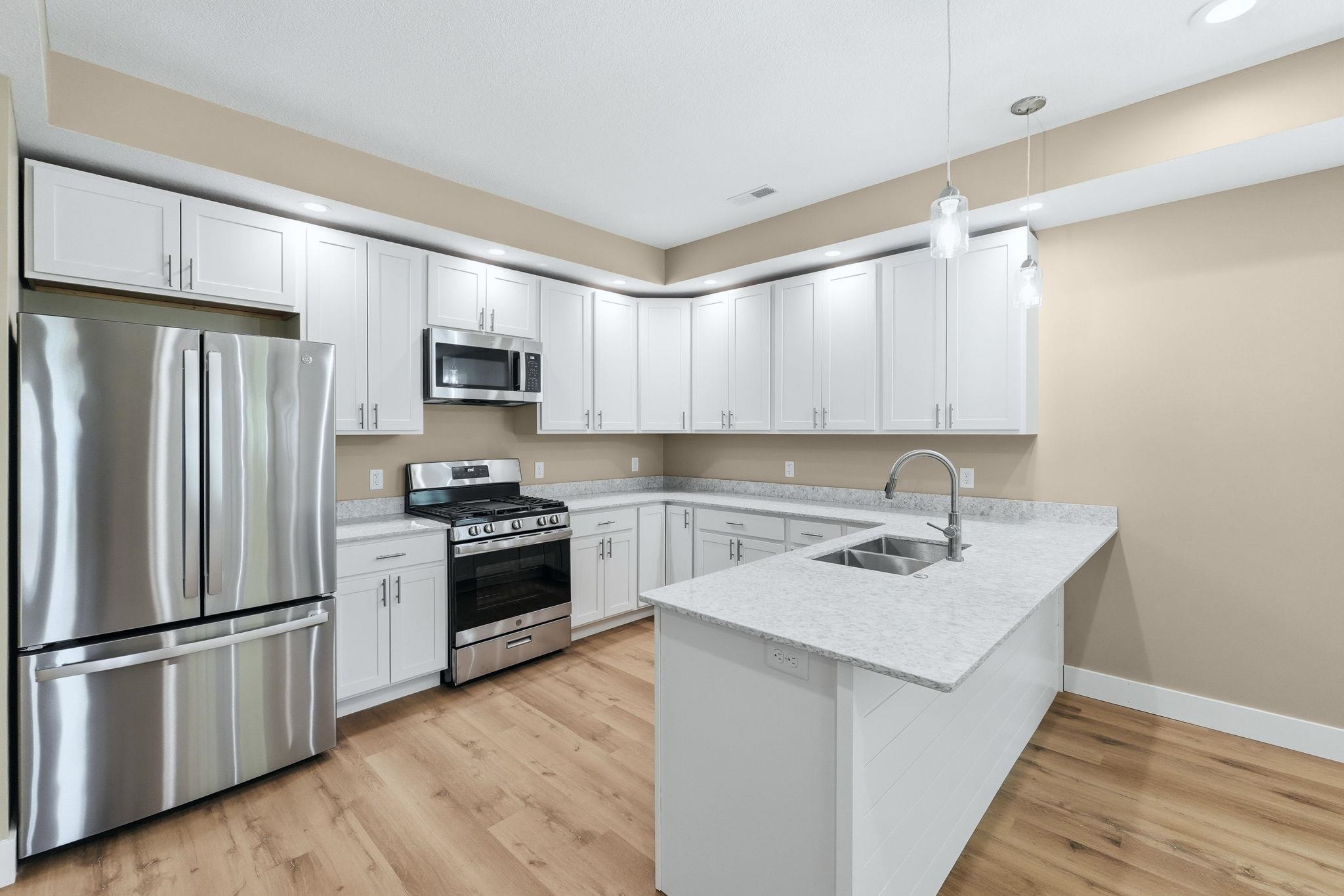 Kitchen featuring wood-finish flooring, white cabinetry, stainless steel appliances, and light-toned countertops