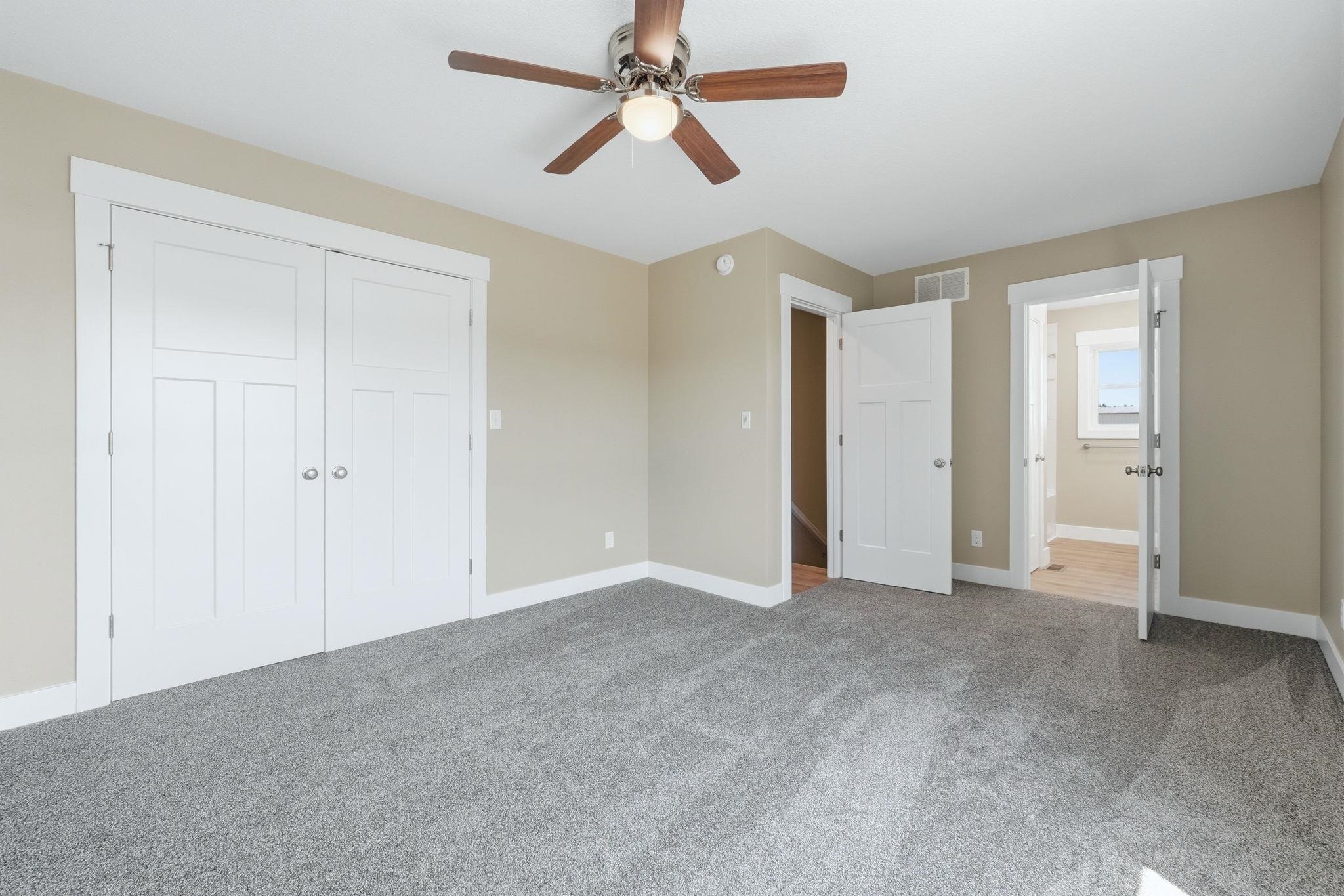 Spacious room featuring neutral paint, gray carpeting, a ceiling fan with integrated lighting, and white trim