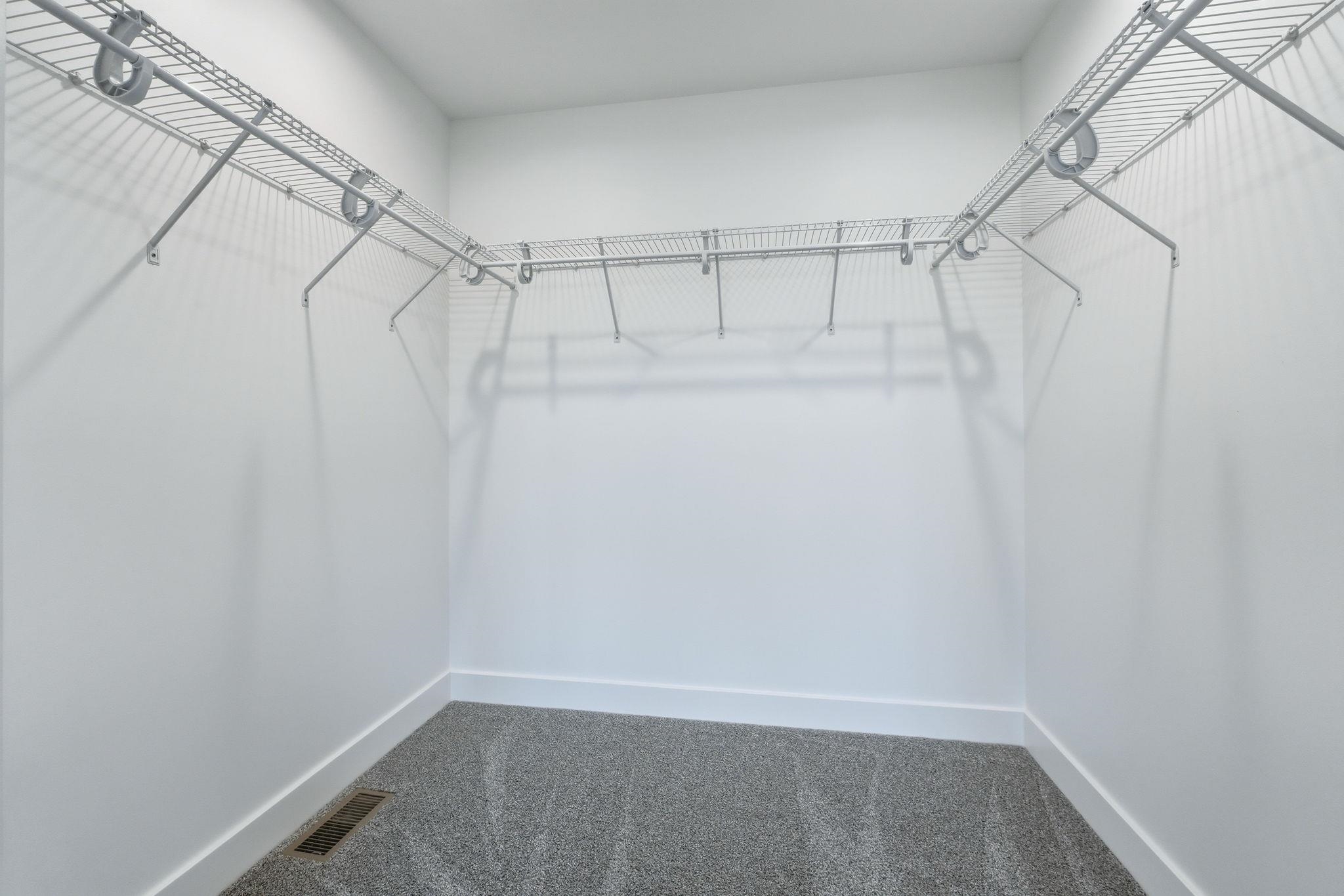 Walk-in closet with wire shelving system and hanging rods, white walls, white baseboards, and gray patterned carpet flooring