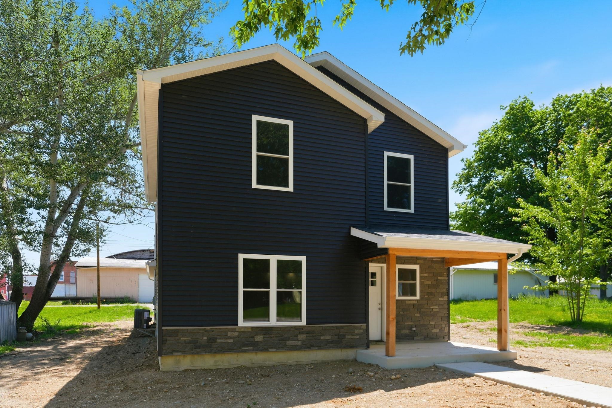Contemporary two-story residence featuring dark siding, white trim, and a stone veneer foundation