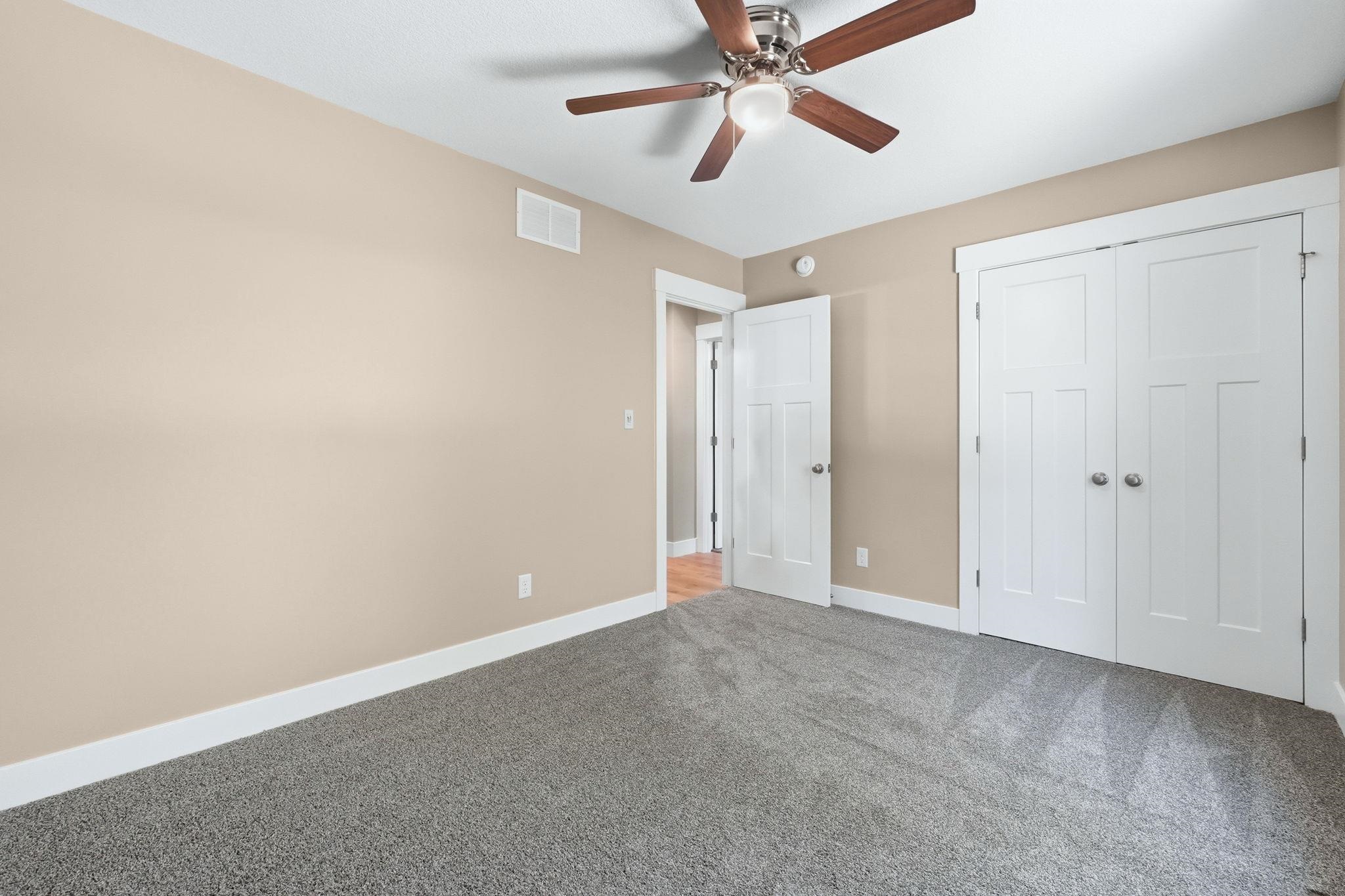 Room featuring neutral tone walls, grey carpet, white trim, and a ceiling fan with integrated lighting