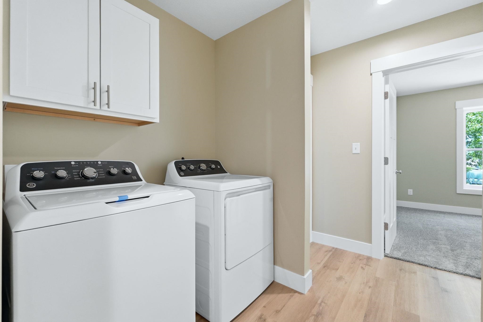 Dedicated laundry area featuring wood-finish flooring, white cabinetry with silver-tone pulls, light tan wall paint, and a recessed ceiling light fixture