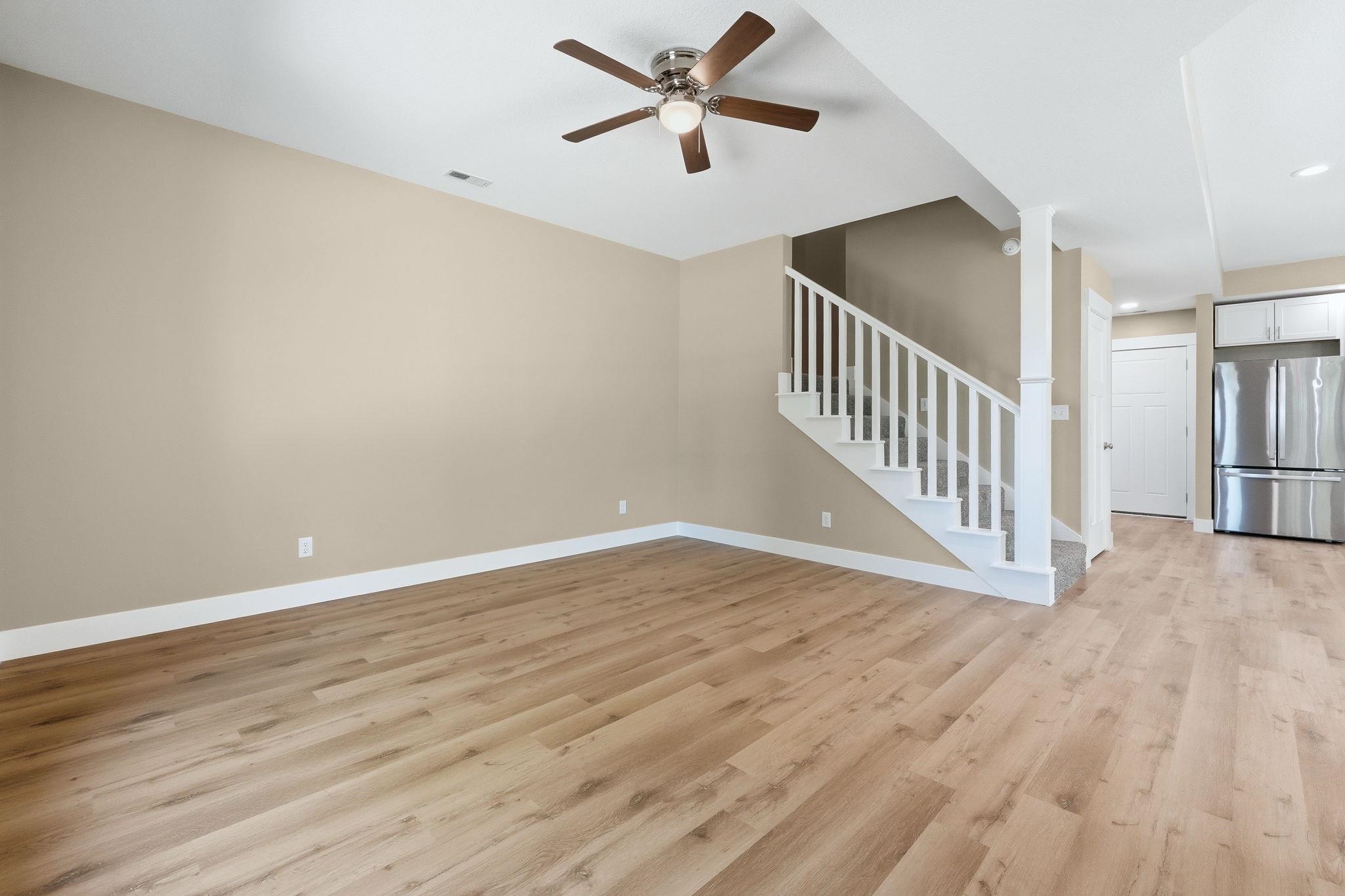 Spacious interior featuring wood-finish flooring, neutral paint palette, a contemporary ceiling fan, white baseboards, and an open staircase with white balusters