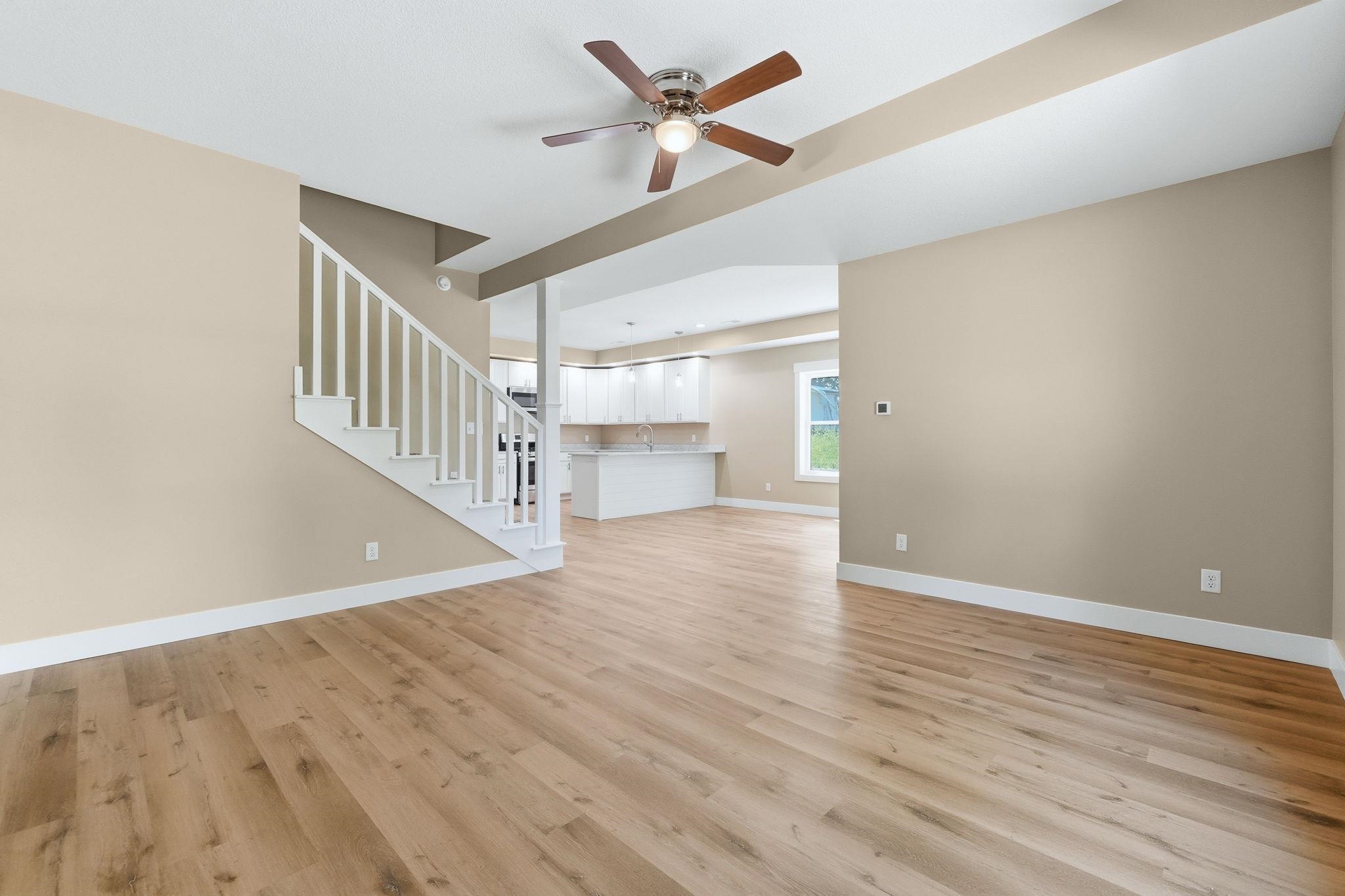 Spacious living area featuring light wood-finish flooring, a ceiling fan, and neutral wall tones