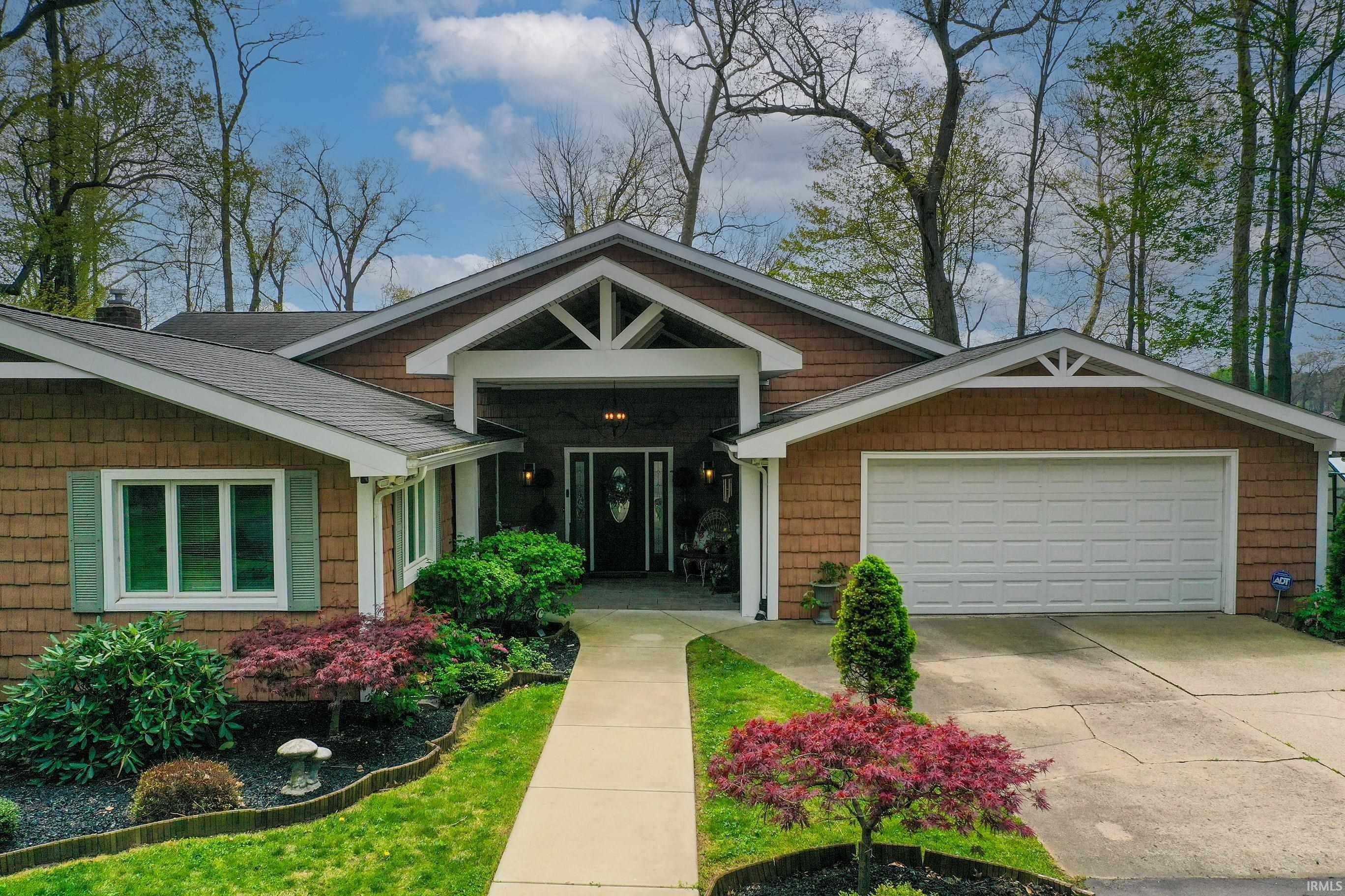 Contemporary ranch-style exterior featuring cedar shake siding, a prominent gabled entryway, a two-car garage, and established landscaping