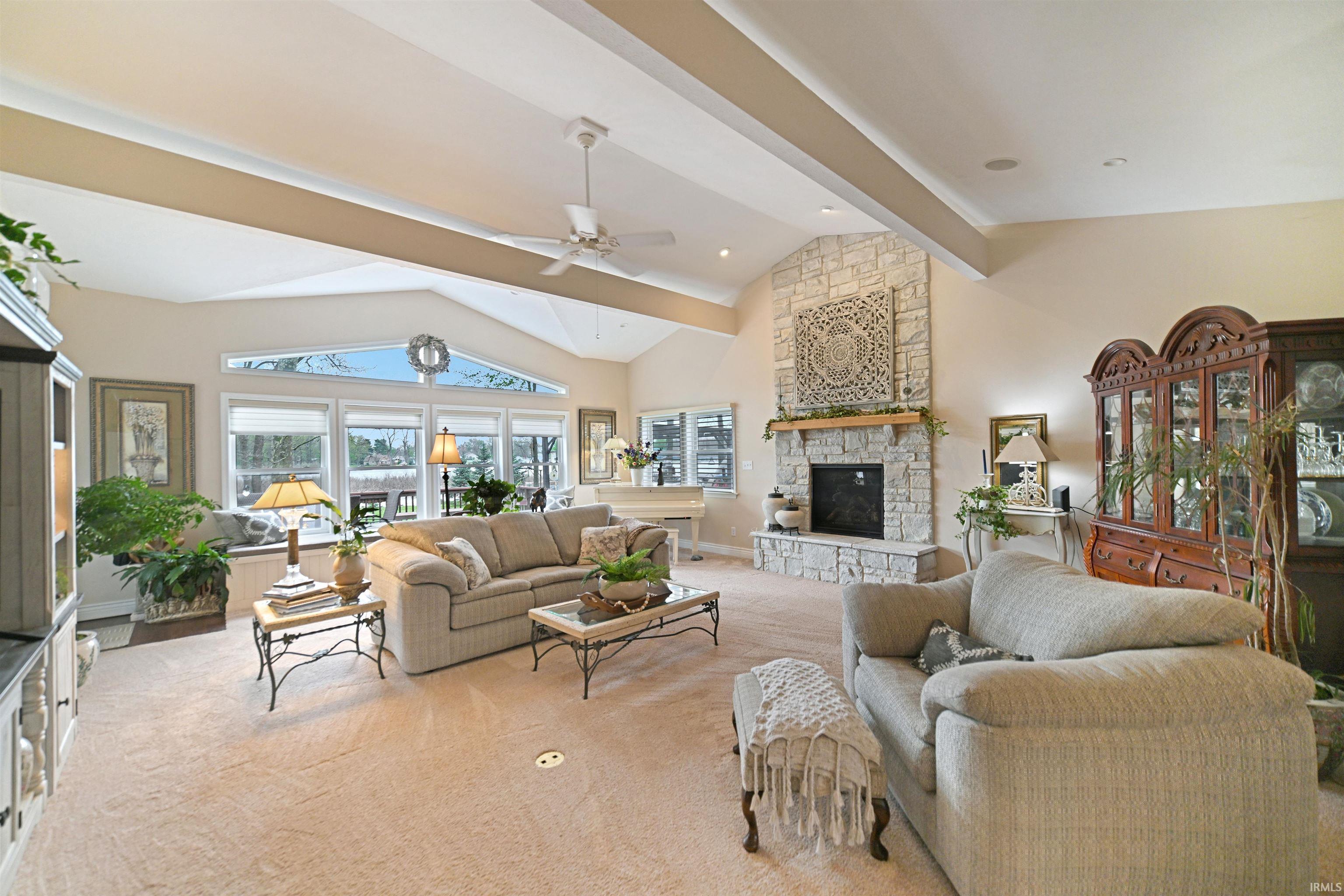 Spacious living area featuring a vaulted ceiling with exposed beams, a stone-clad fireplace, and expansive windows