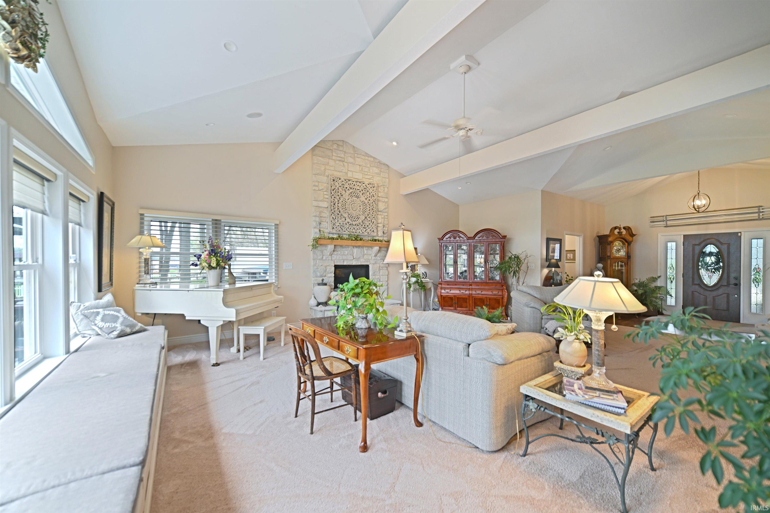 Expansive living space featuring a stone-clad fireplace with a decorative mantel, vaulted ceilings with exposed beams, and a ceiling fan