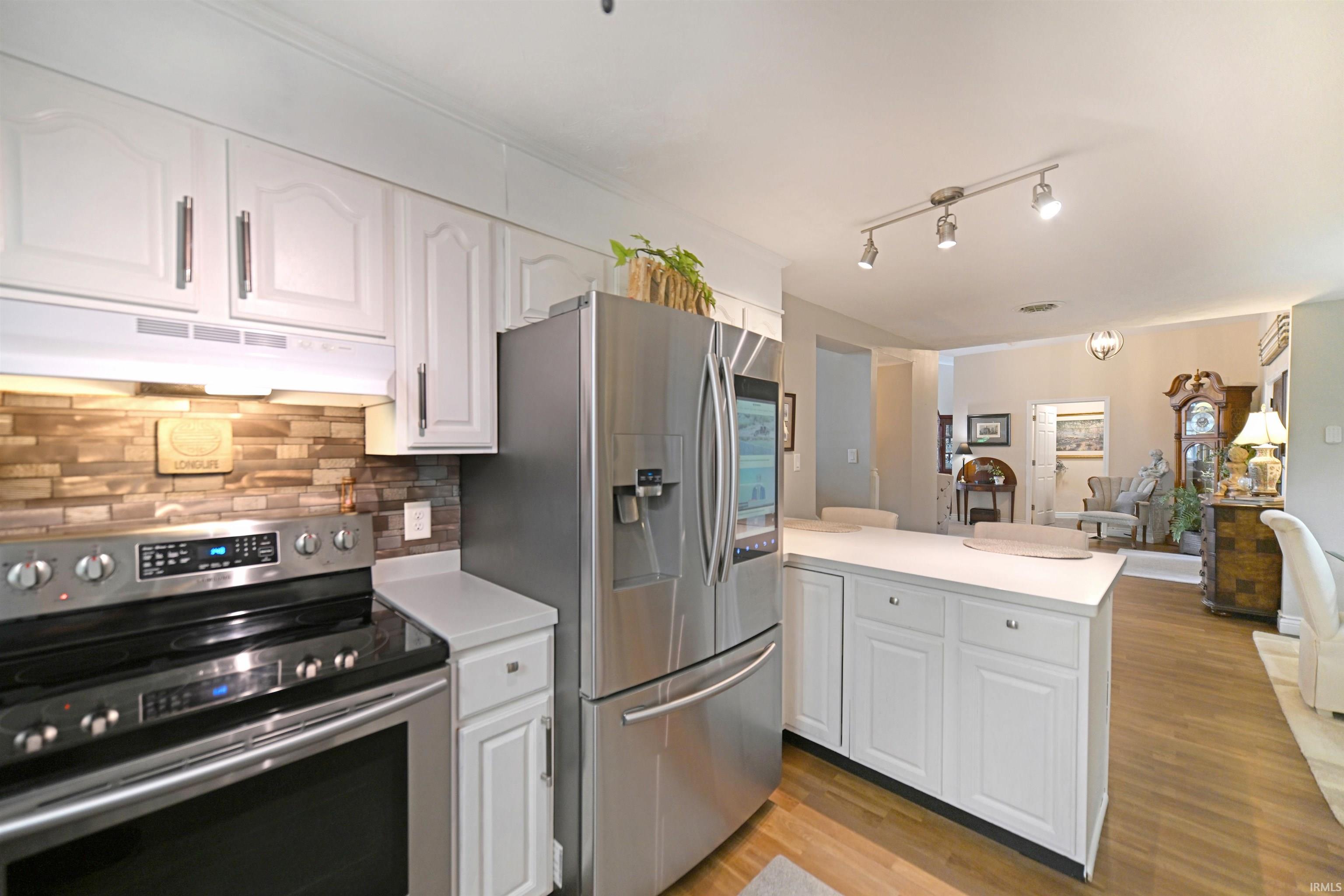 Kitchen featuring white cabinetry, stone-look tile backsplash, stainless steel appliances, and a central island with white countertops