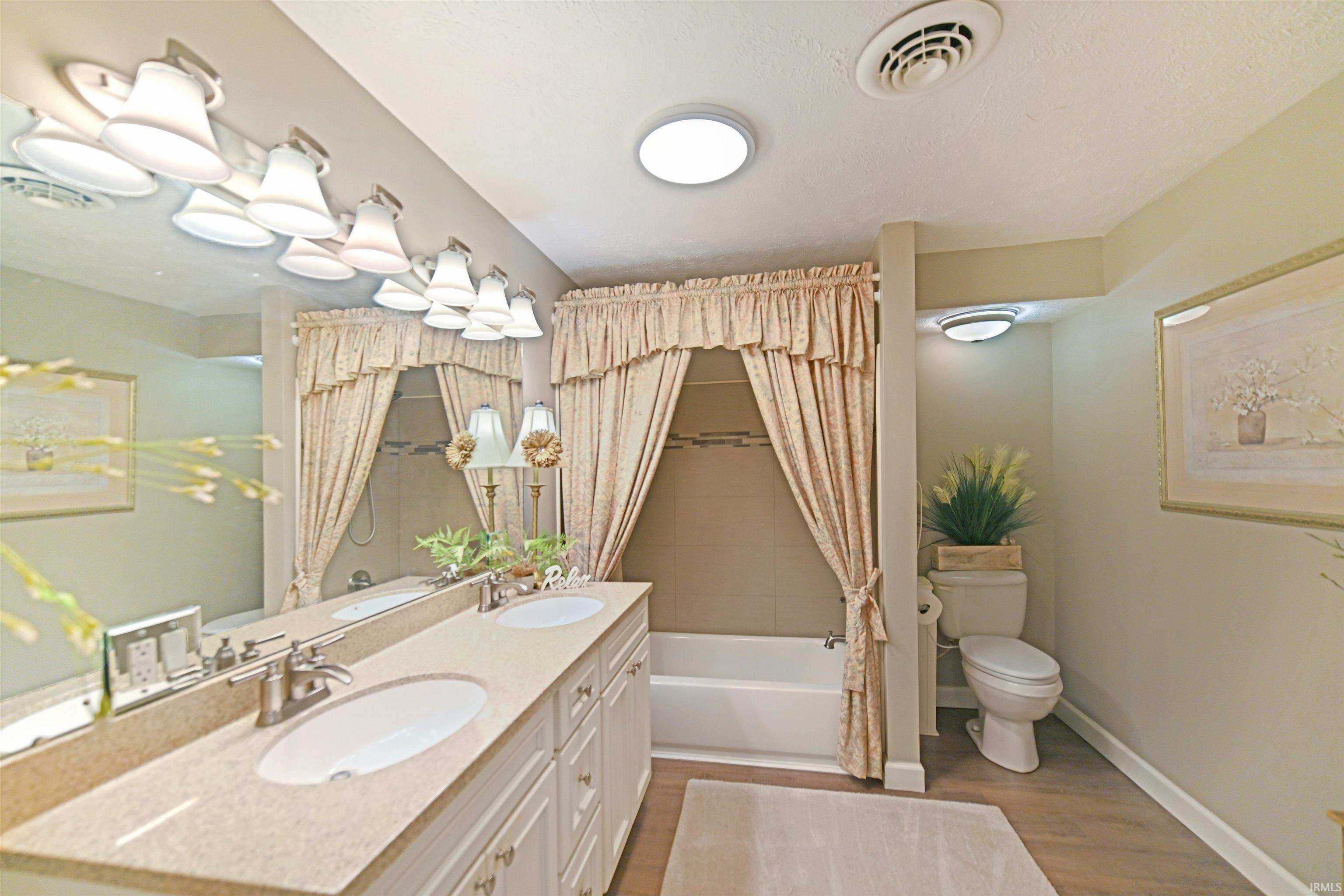 Dual vanity with integrated sinks, brushed nickel fixtures, a full-width mirror, and a generously sized bathtub with tiled surround