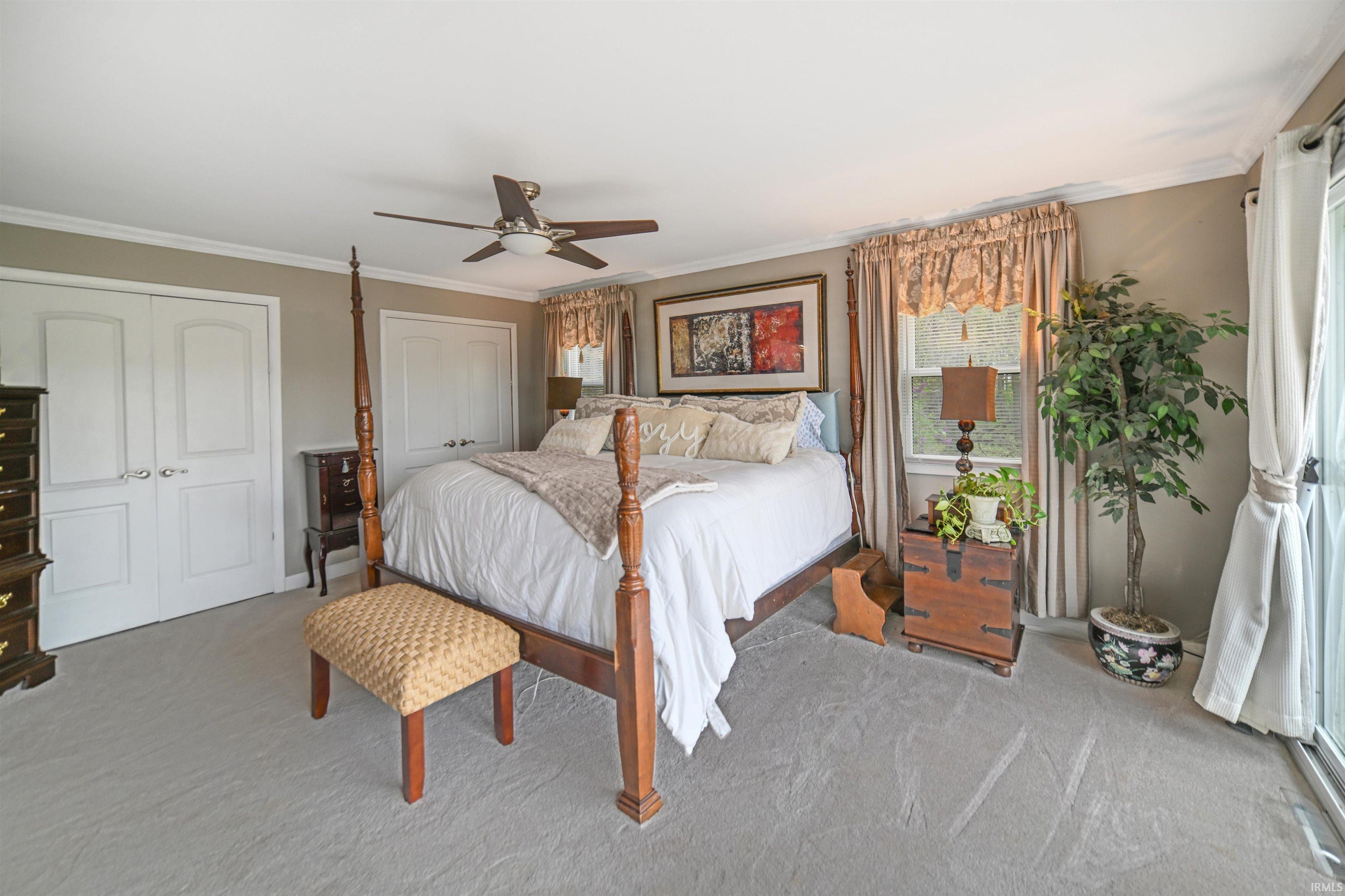 Spacious bedroom featuring light gray carpeting, crown molding, a ceiling fan, dual white panel doors, and a glass sliding door providing exterior access