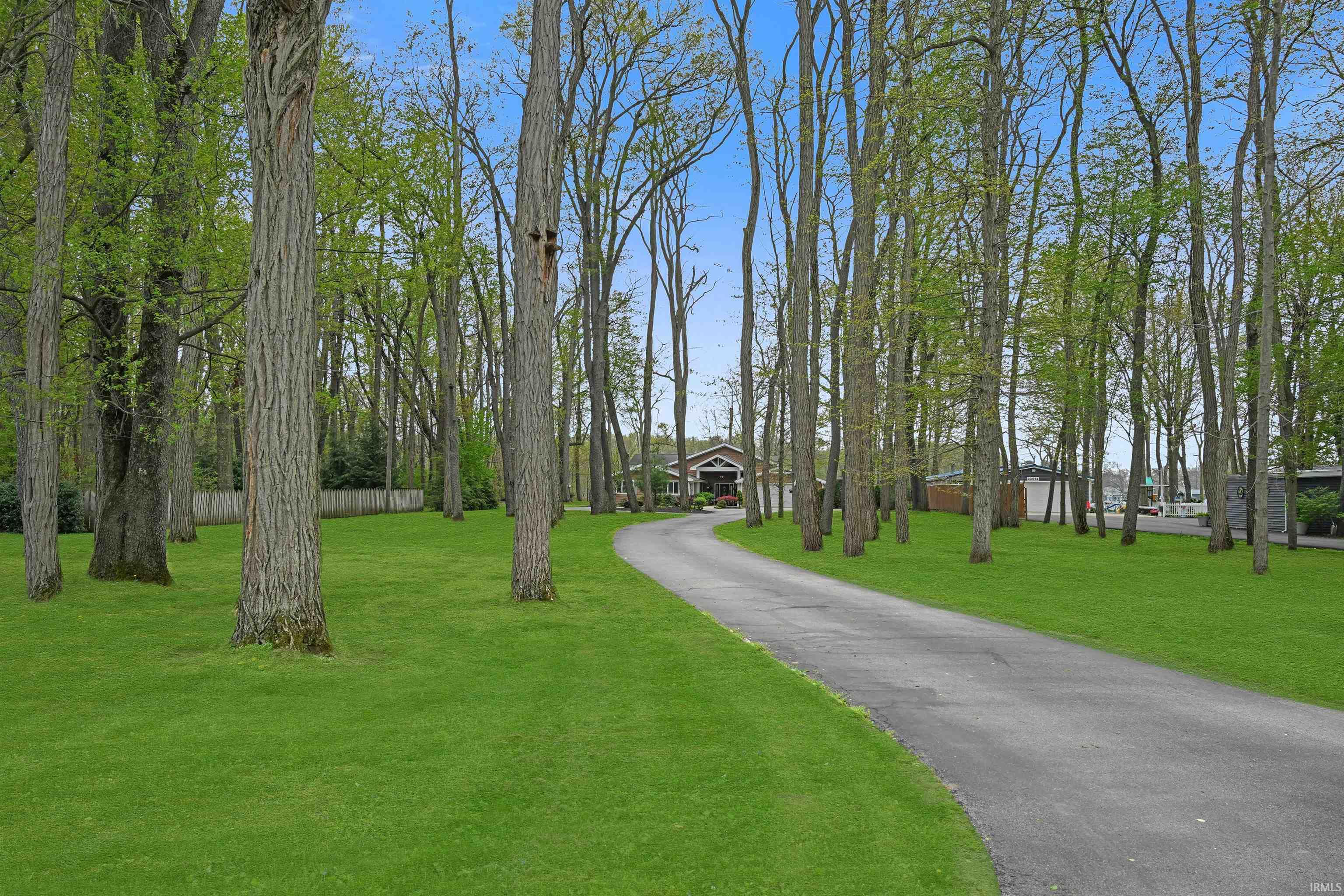 Paved drive approaching a residence, surrounded by mature trees and expansive green lawn