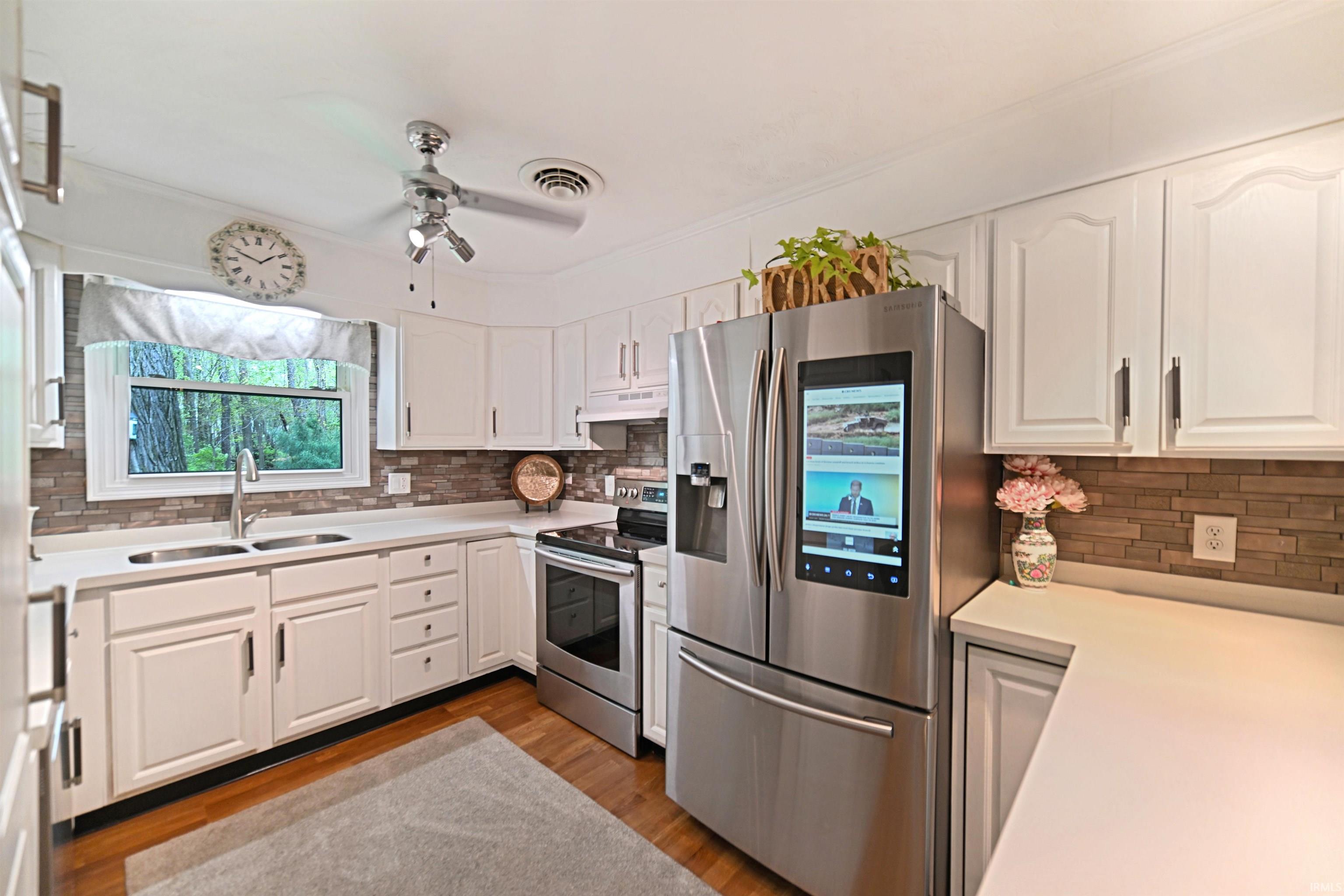 Kitchen featuring a double basin sink, stainless steel appliances, white cabinetry, wood-finish flooring, and a tile backsplash