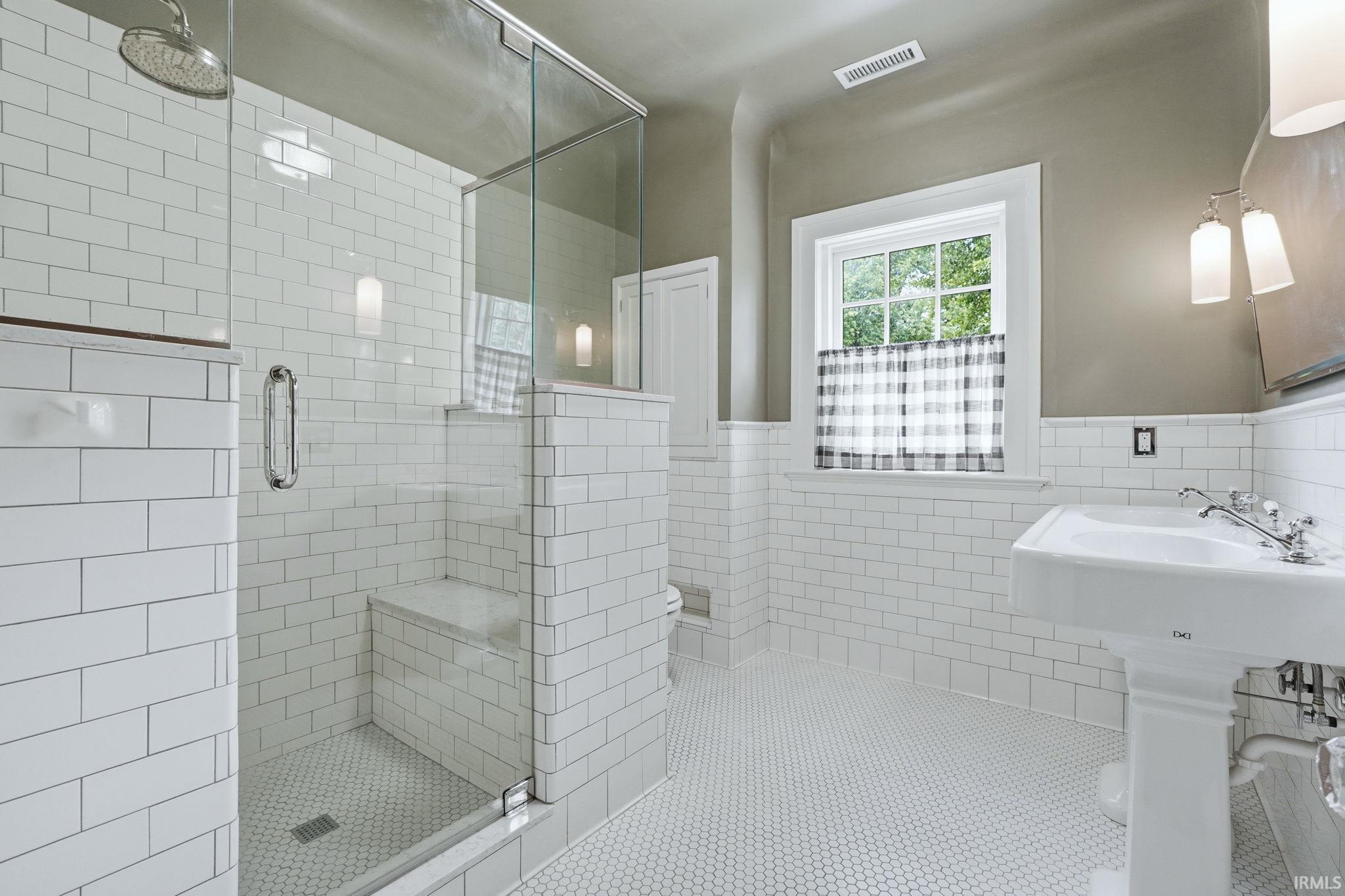 White subway tile walls with a glass-enclosed shower featuring a built-in bench and a rainfall showerhead