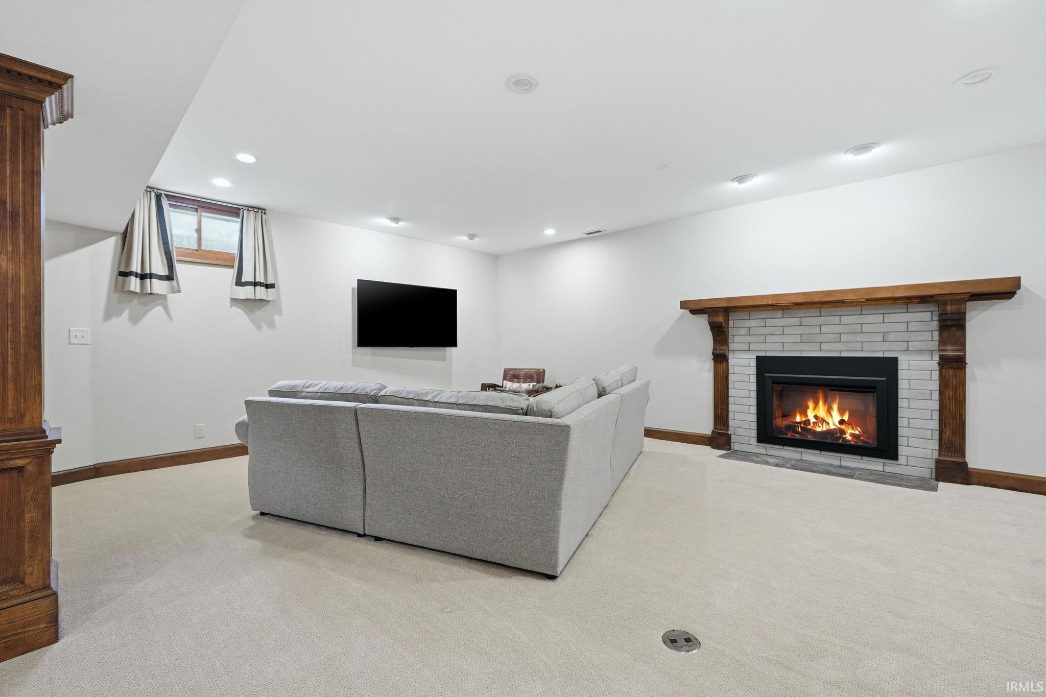Living area featuring a white brick fireplace with a wood mantel, recessed lighting, and light-colored carpeting