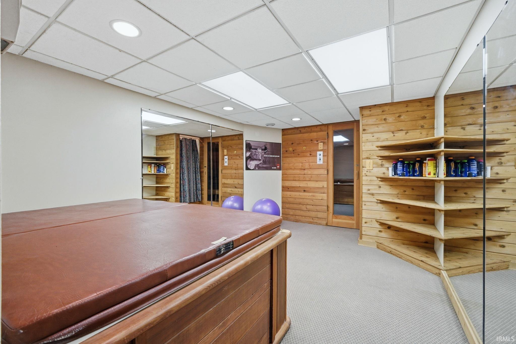 Recreational space featuring a built-in hot tub with a brown cover, wood paneling, corner shelving, and mirrored walls