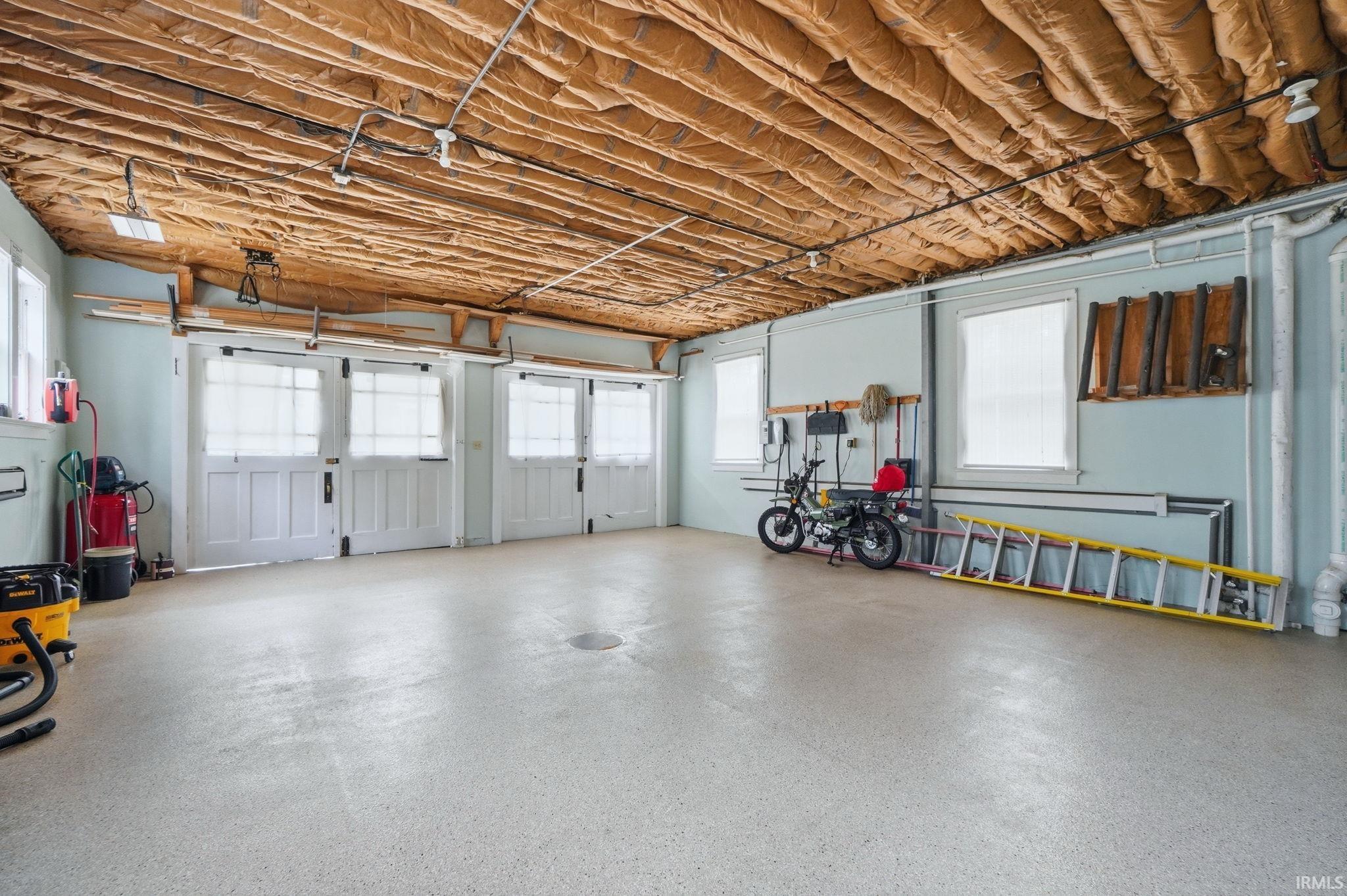 Spacious garage featuring a durable epoxy floor, multiple windows for natural light, and exposed insulation for potential finishing