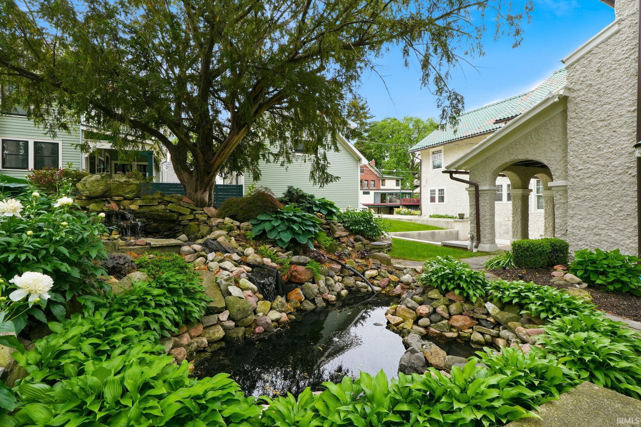 Landscaped garden featuring a tiered waterfall, a tranquil pond, mature trees, and vibrant hostas