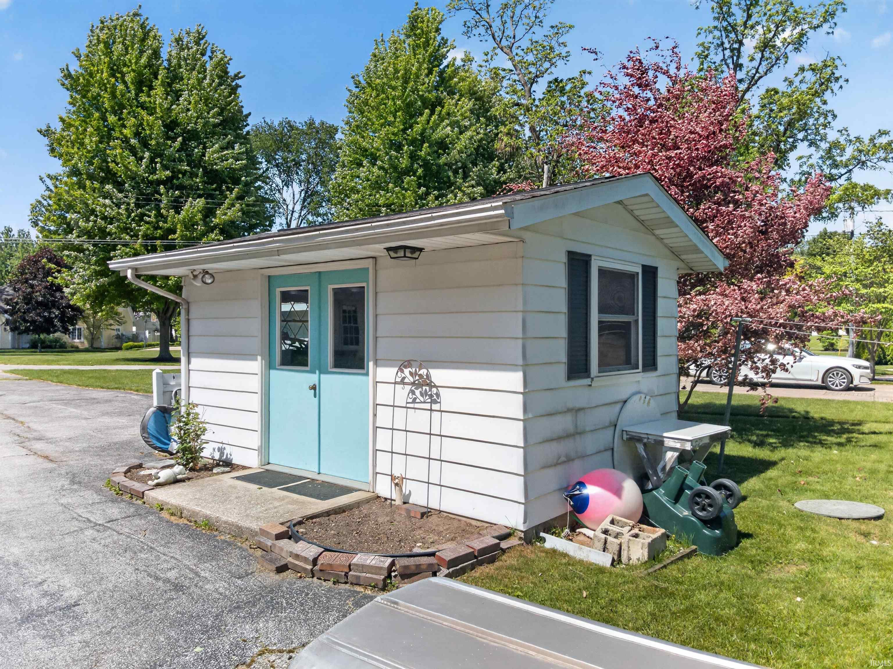 Detached outbuilding with white siding, light blue double doors, and a side window with dark shutters