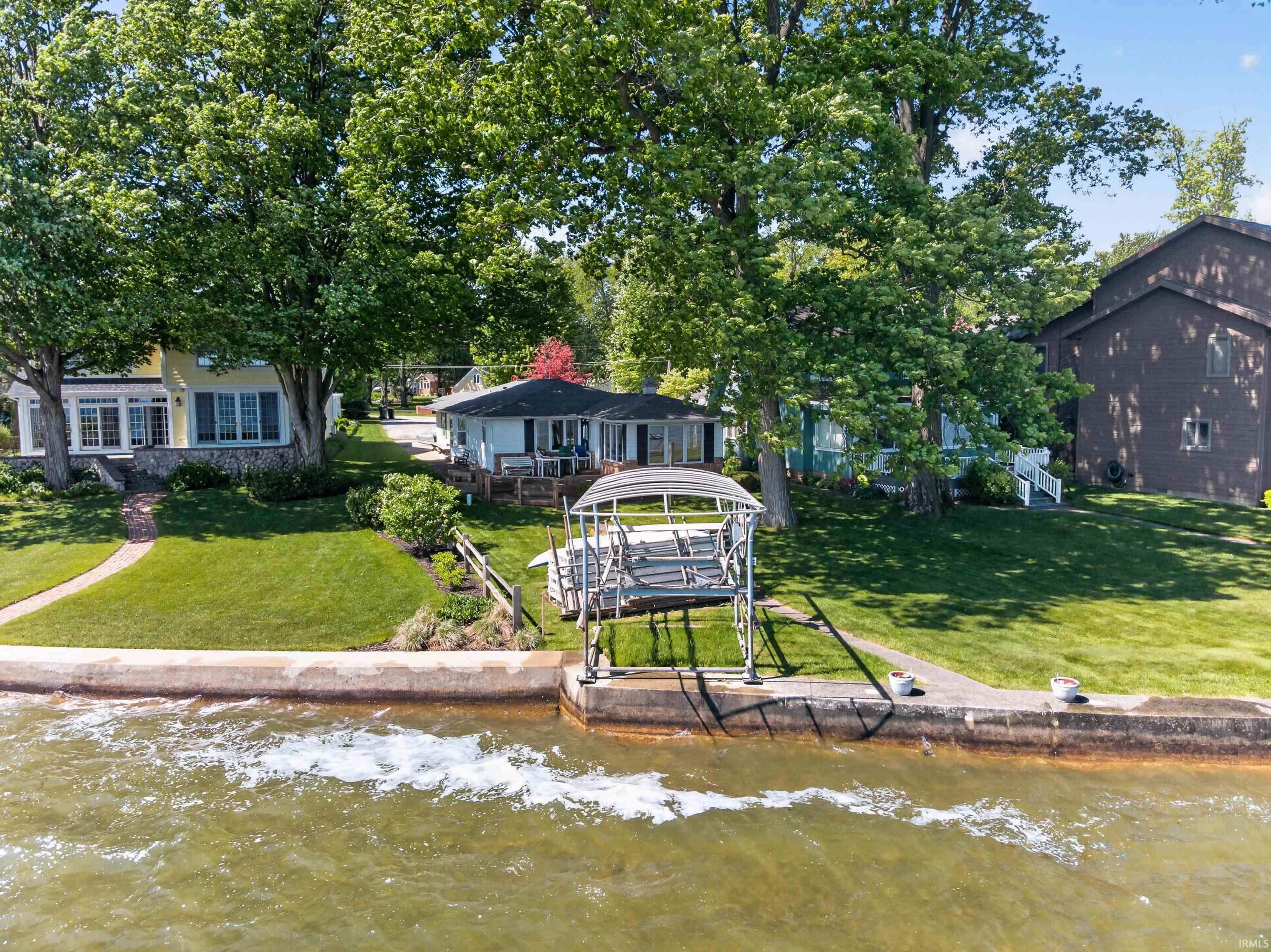 Waterfront property featuring a boat lift, concrete seawall, and a manicured lawn leading to the water