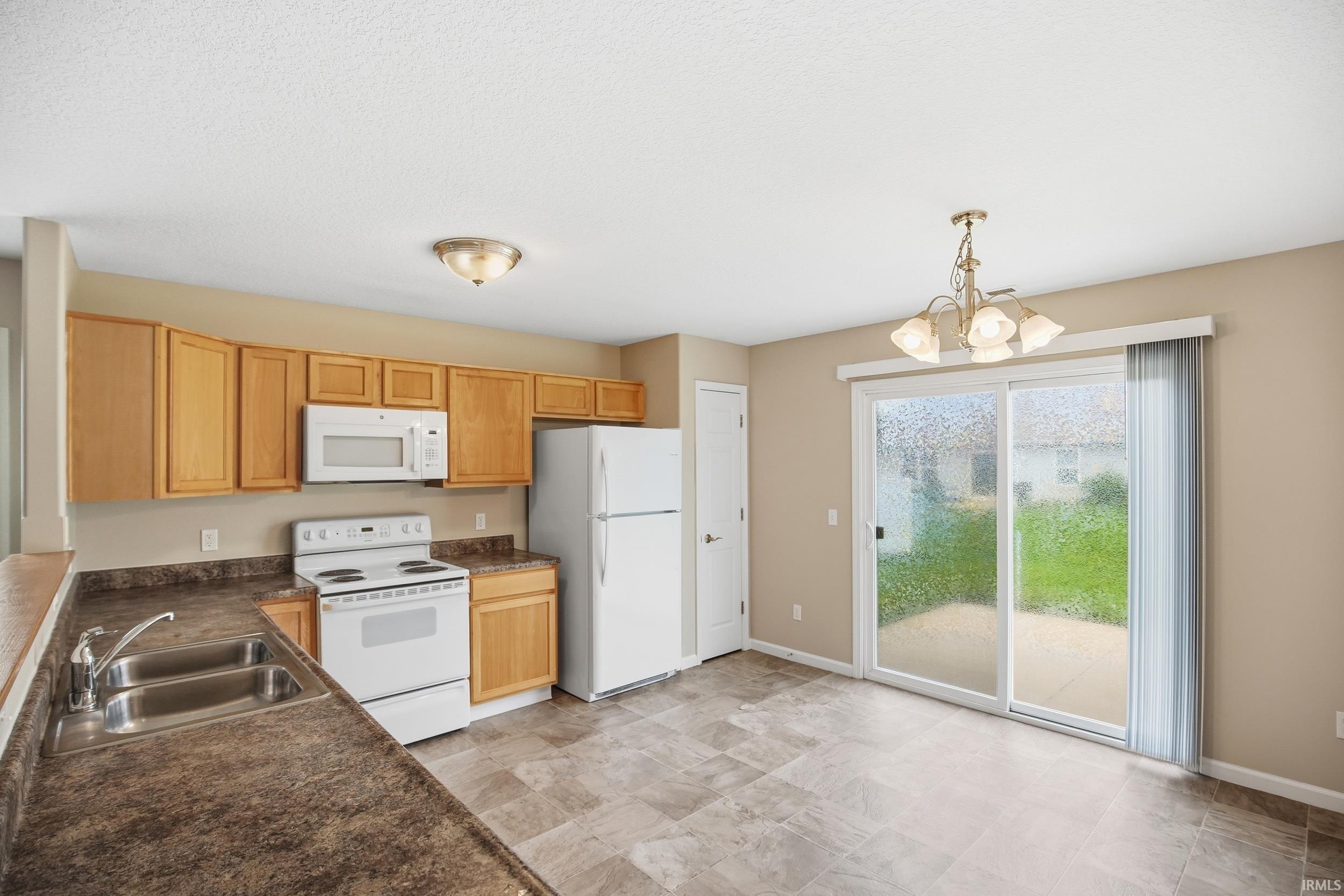 Kitchen and dining area featuring light wood cabinetry, white appliances, a double basin sink, and a sliding glass door providing access to an outdoor patio