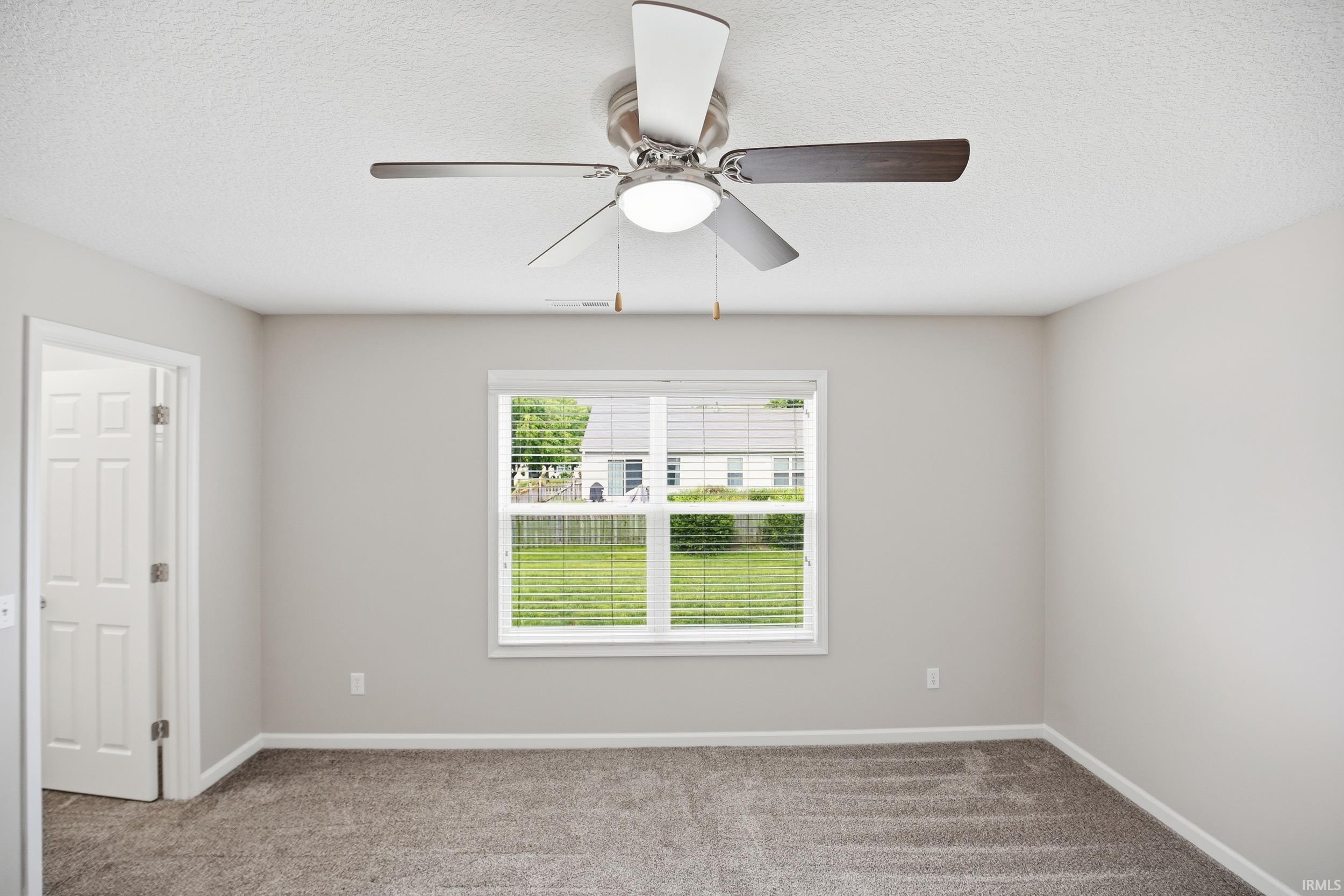 Neutral-toned room featuring a ceiling fan with integrated lighting, a window with horizontal blinds, light gray walls, and textured carpet flooring