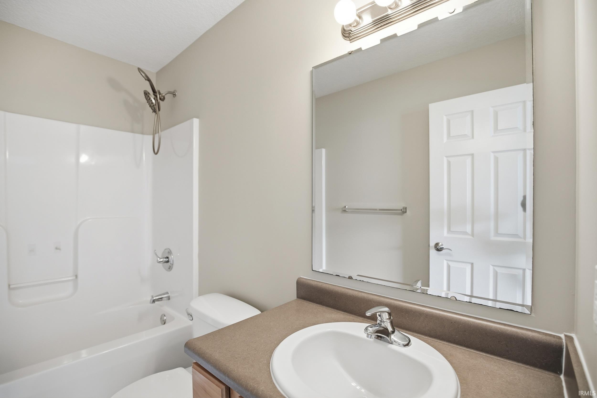 Bathroom featuring a white bathtub and shower surround, a vanity with a drop-in sink, a large wall-mounted mirror, and a wall-mounted light fixture