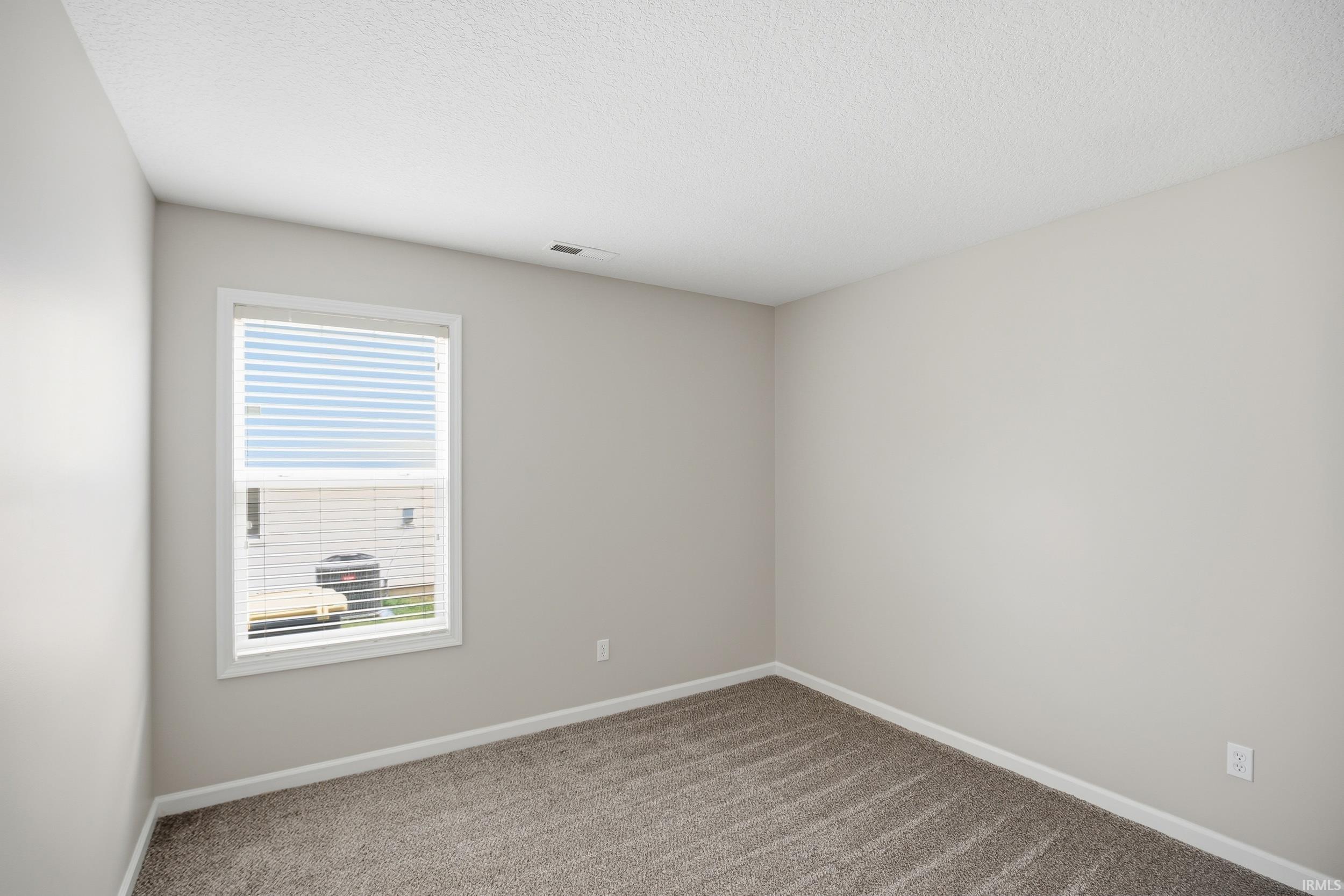 Neutral-toned room featuring a single window with blinds, light gray walls, and textured carpeting