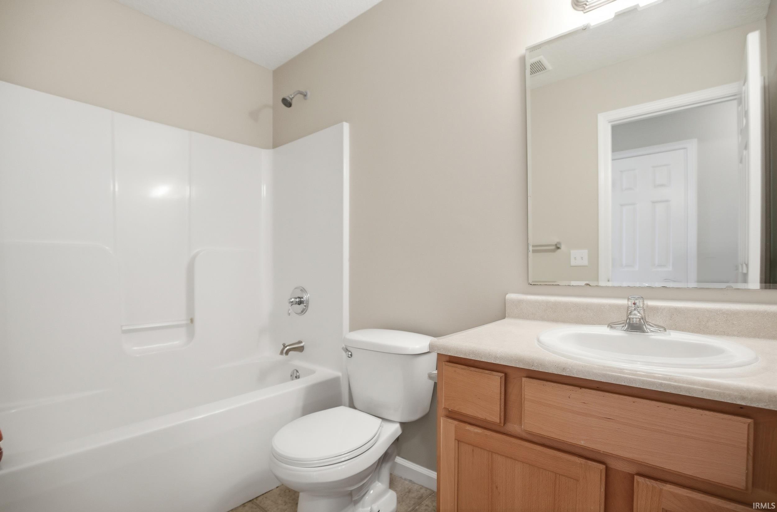 Bathroom featuring a white tub and shower surround, chrome fixtures, a light-toned vanity with an integrated sink, a large wall-mounted mirror, and neutral wall paint
