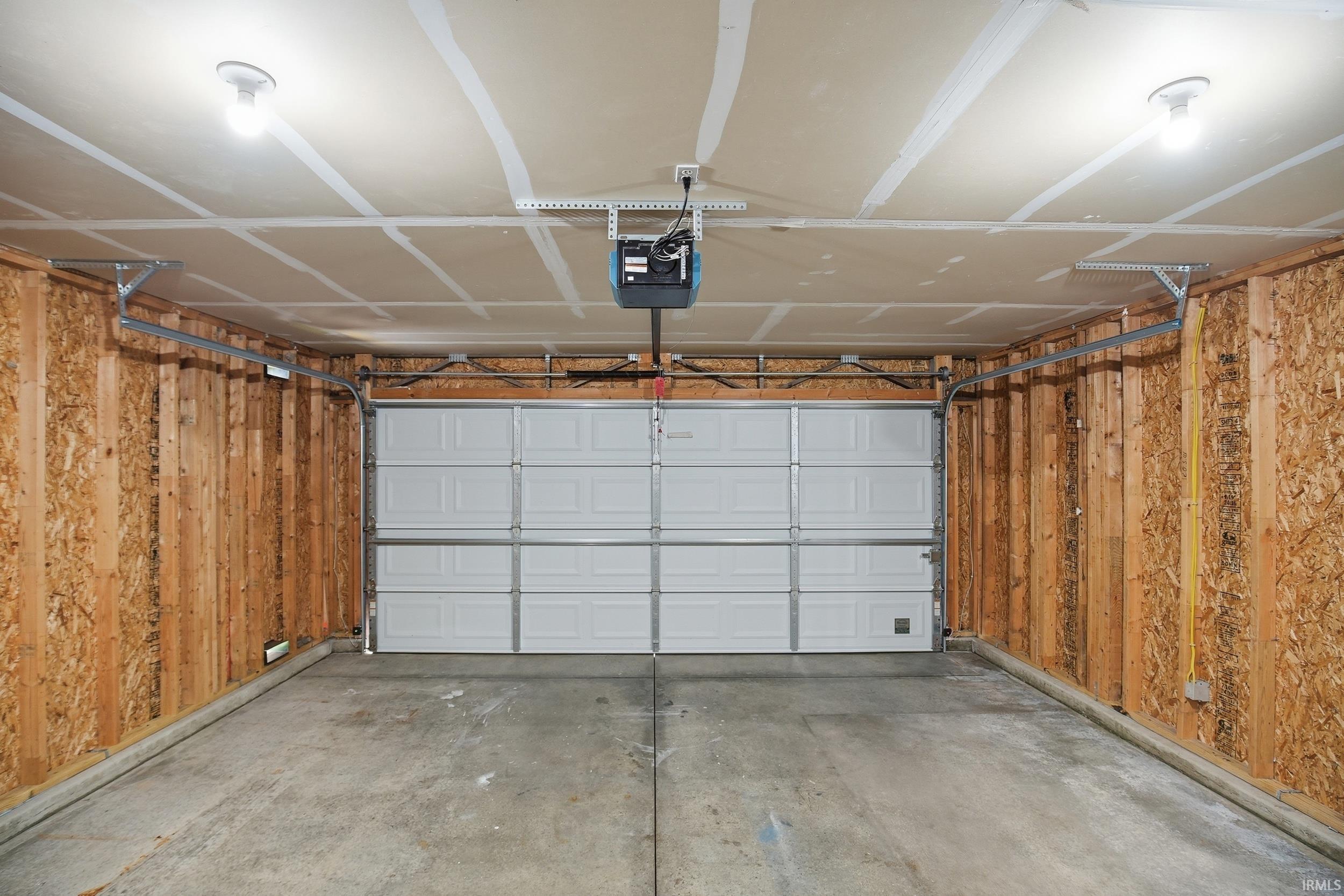 Attached two-car garage featuring a white panel door, concrete flooring, and bare wood-finish walls