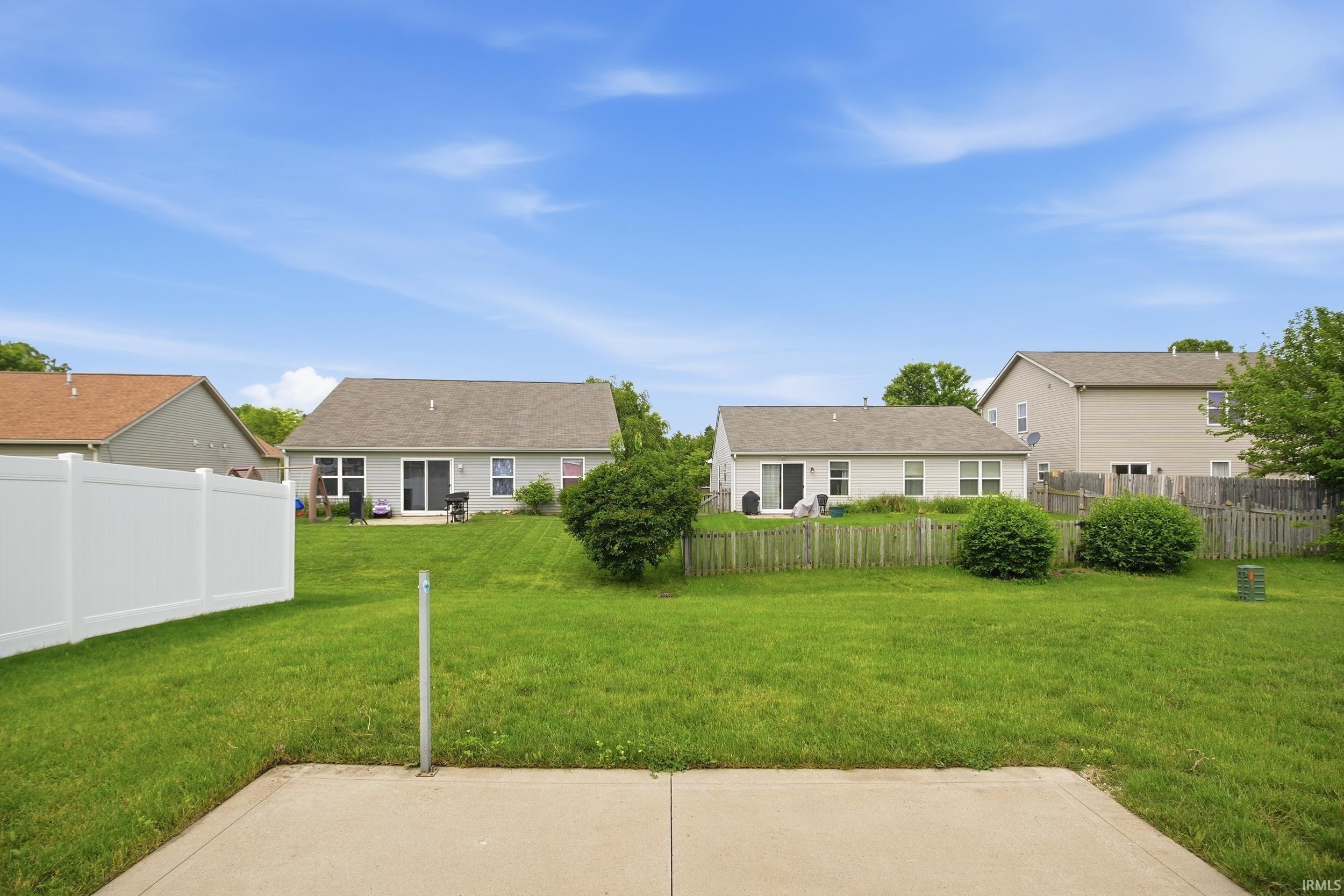 Expansive grass lawn featuring a concrete patio, white vinyl fencing, and mature shrubbery