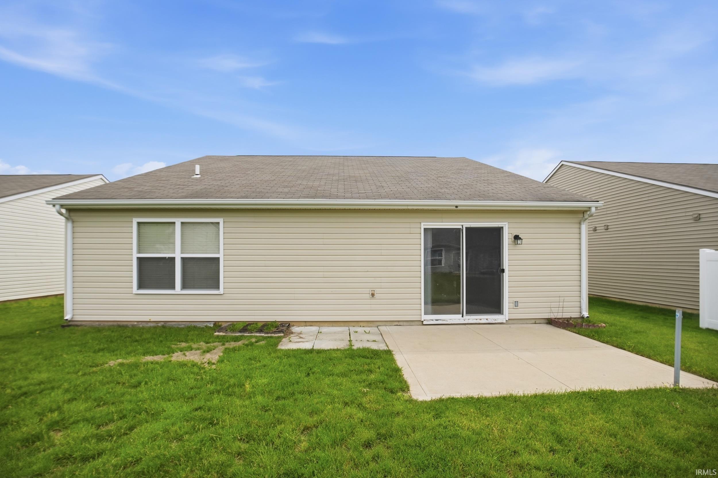 Rear exterior featuring a sliding glass door, a window with white trim, and a concrete patio