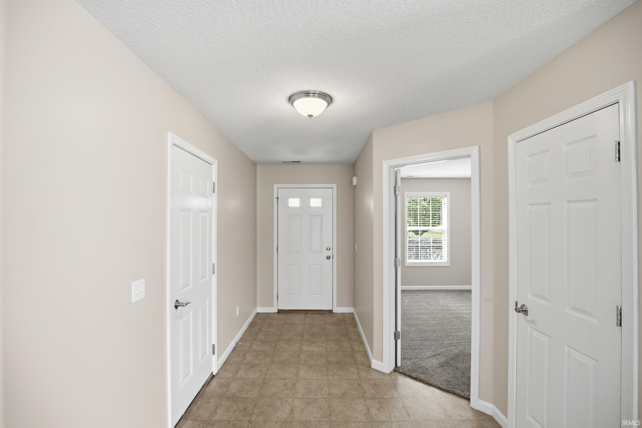 Entrance foyer featuring neutral tone walls, tile flooring, white six-panel doors, and a flush-mount ceiling light