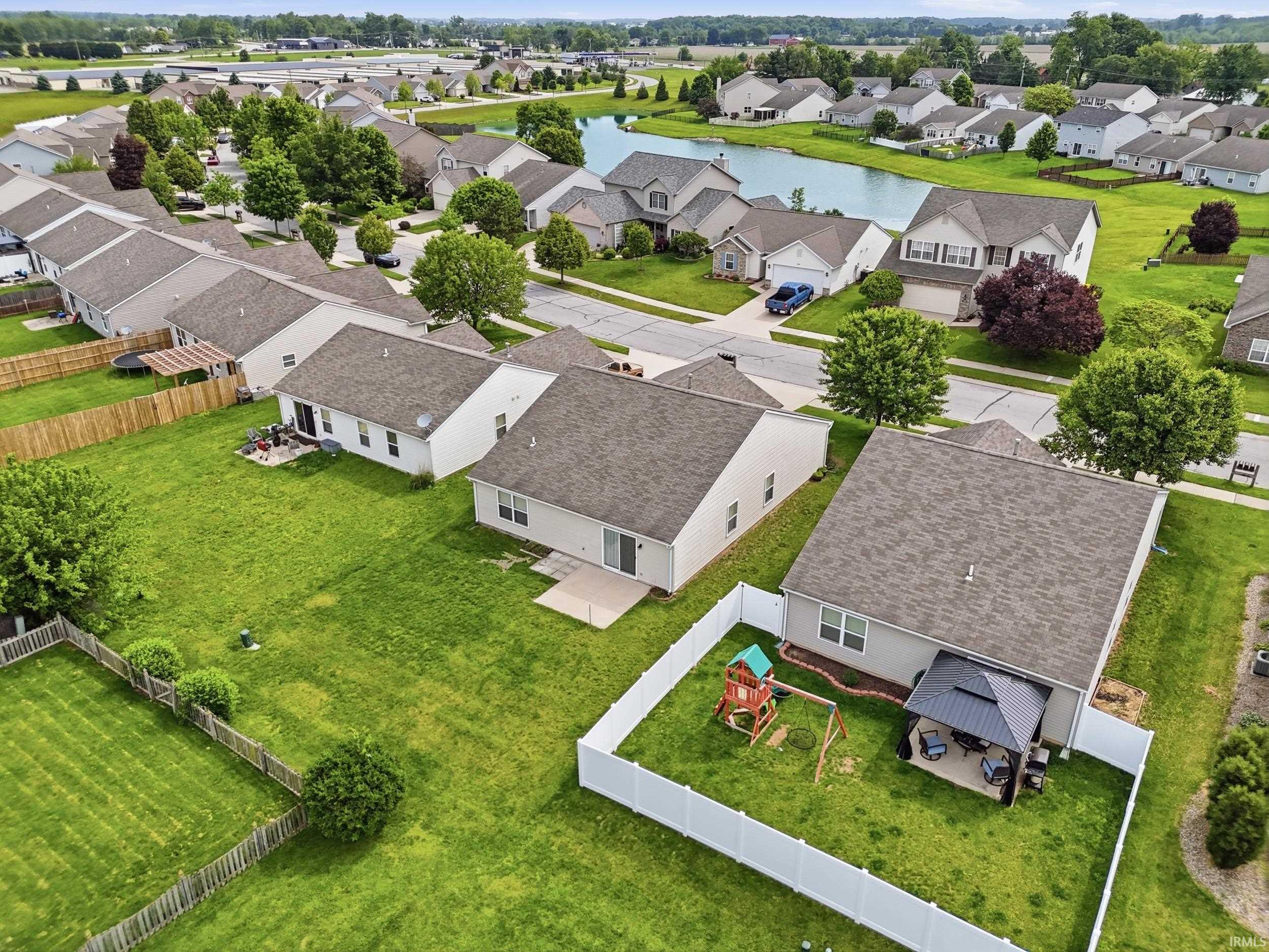 Aerial view showcasing residential properties with a water feature, paved streets, and green spaces