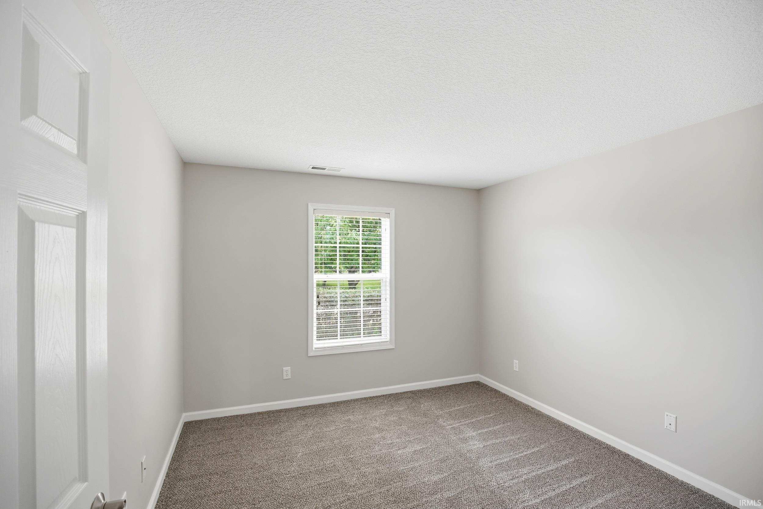Bedroom featuring neutral gray walls, textured carpeting, white baseboards, and a double-pane window with white blinds